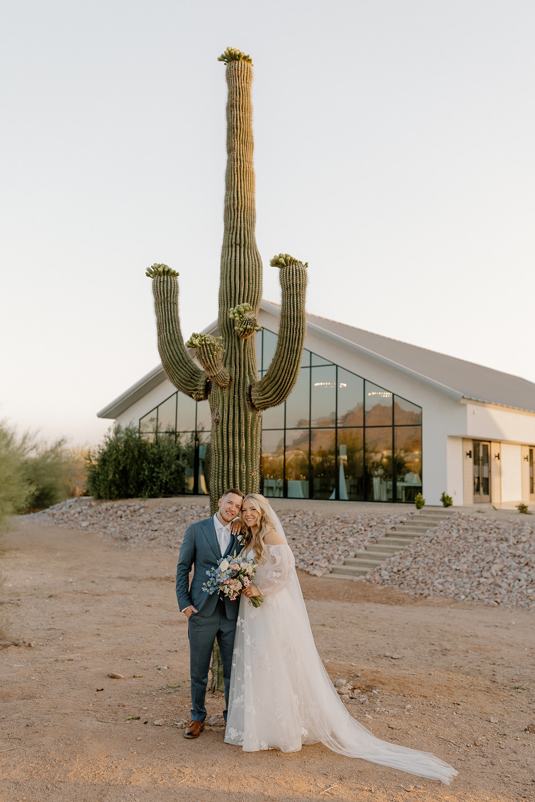 Newly married couple standing together smiling joyfully in front of tall cactus after Desert View wedding