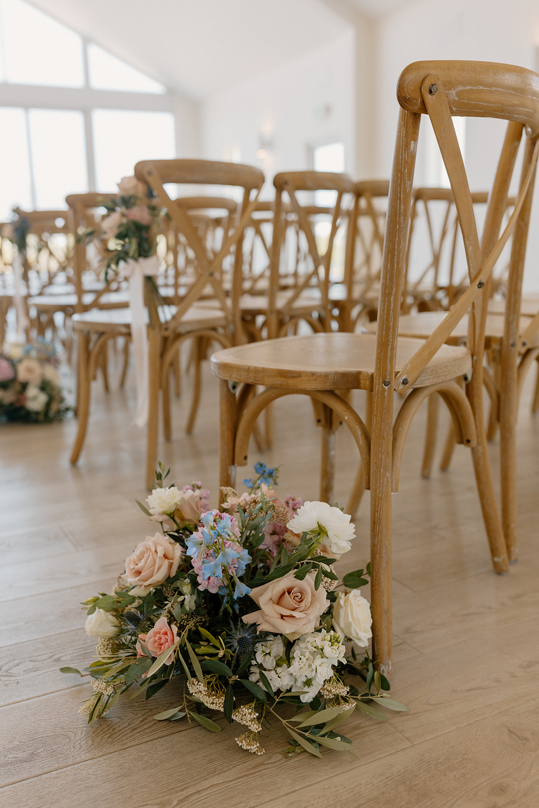 Close up of wooden chairs and floral arrangements on the ground at ceremony location. 