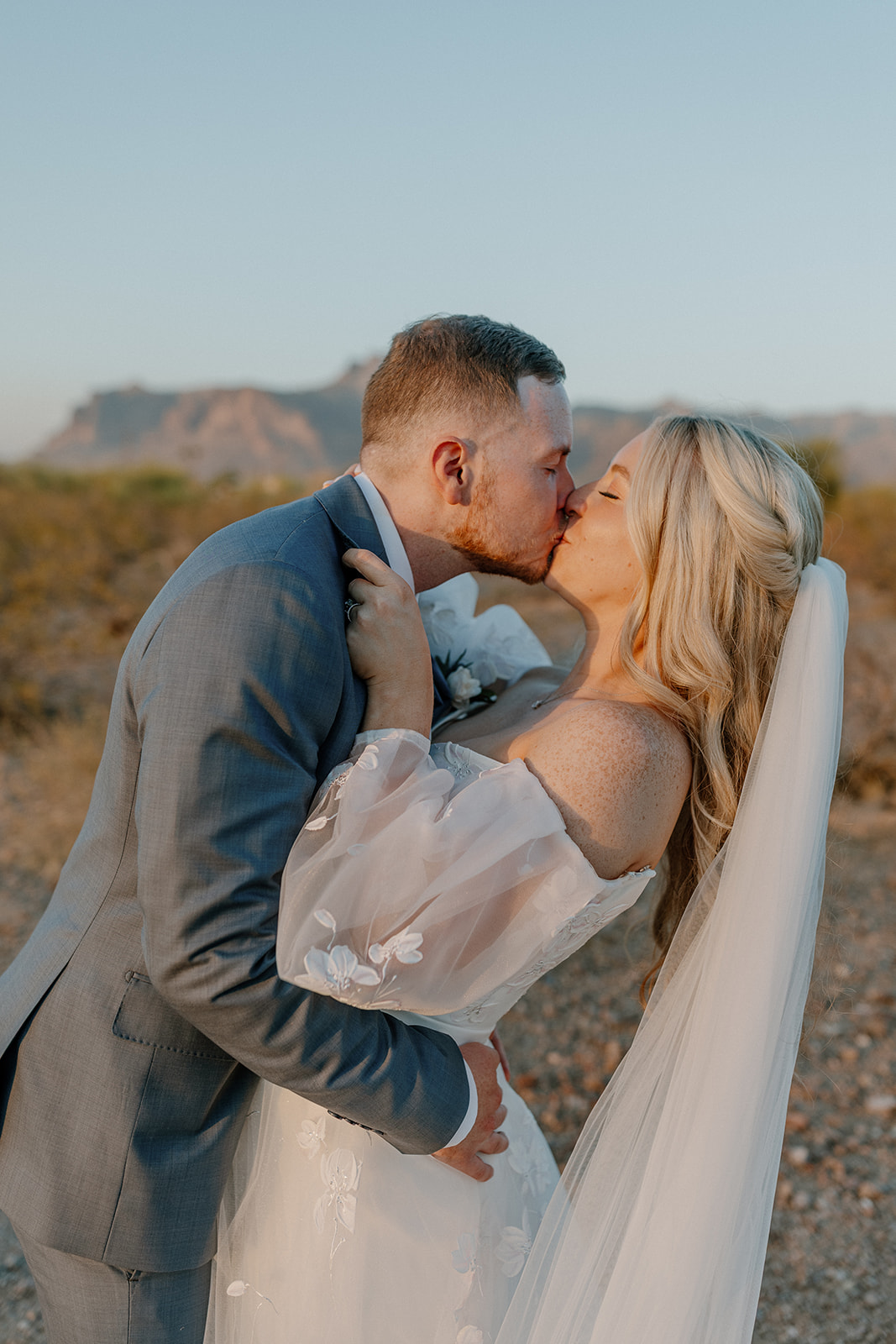 Bride grips Groom's lapels and brings him in for a passionate kiss during their bridal portraits after desert view wedding