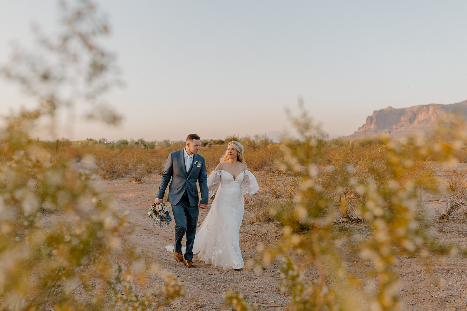 Newly married couple walking hand in hand through desert area after intimate wedding ceremony. 
