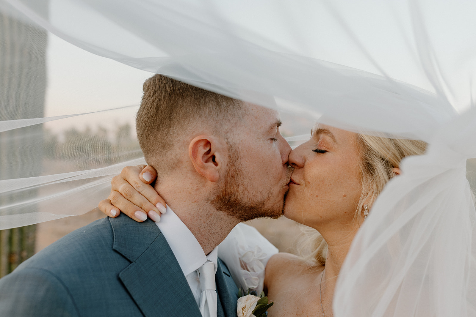 Newly married couple kiss under bride's veil as it blows in the wind. 