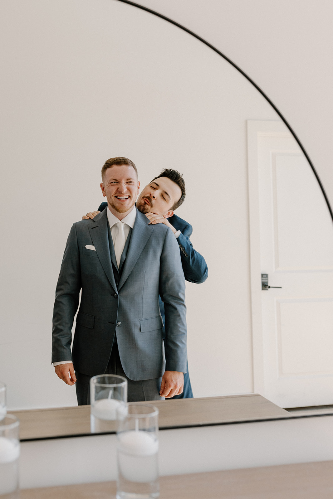 Groomsmen helping groom get ready for wedding by making him laugh and helping put on his jacket. 