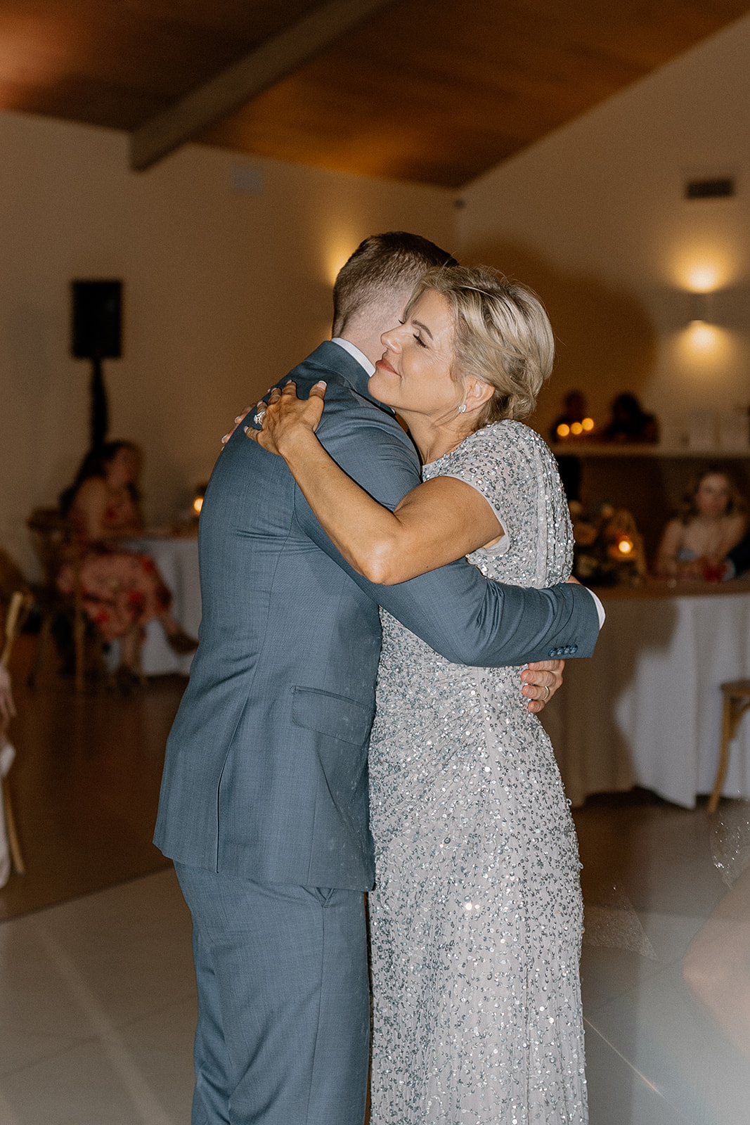 Groom's mom embraces groom while they dance together during mother son dance. 
