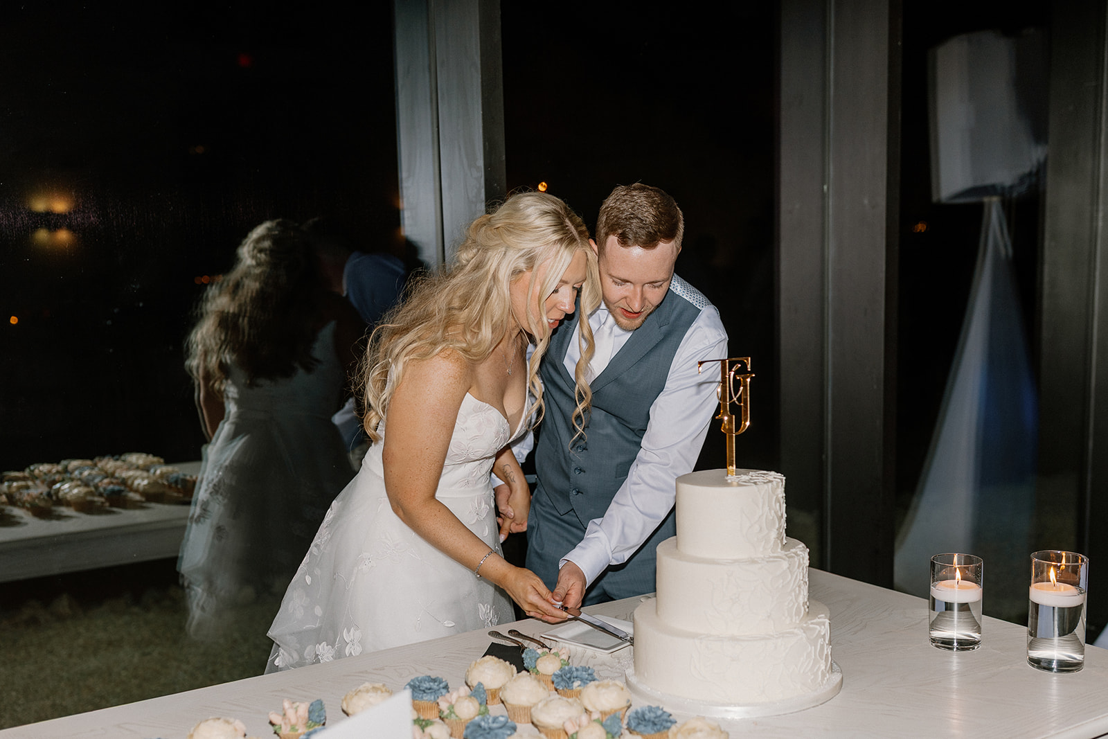 Newly married husband and wife cut three tier white wedding cake together to celebrate. 