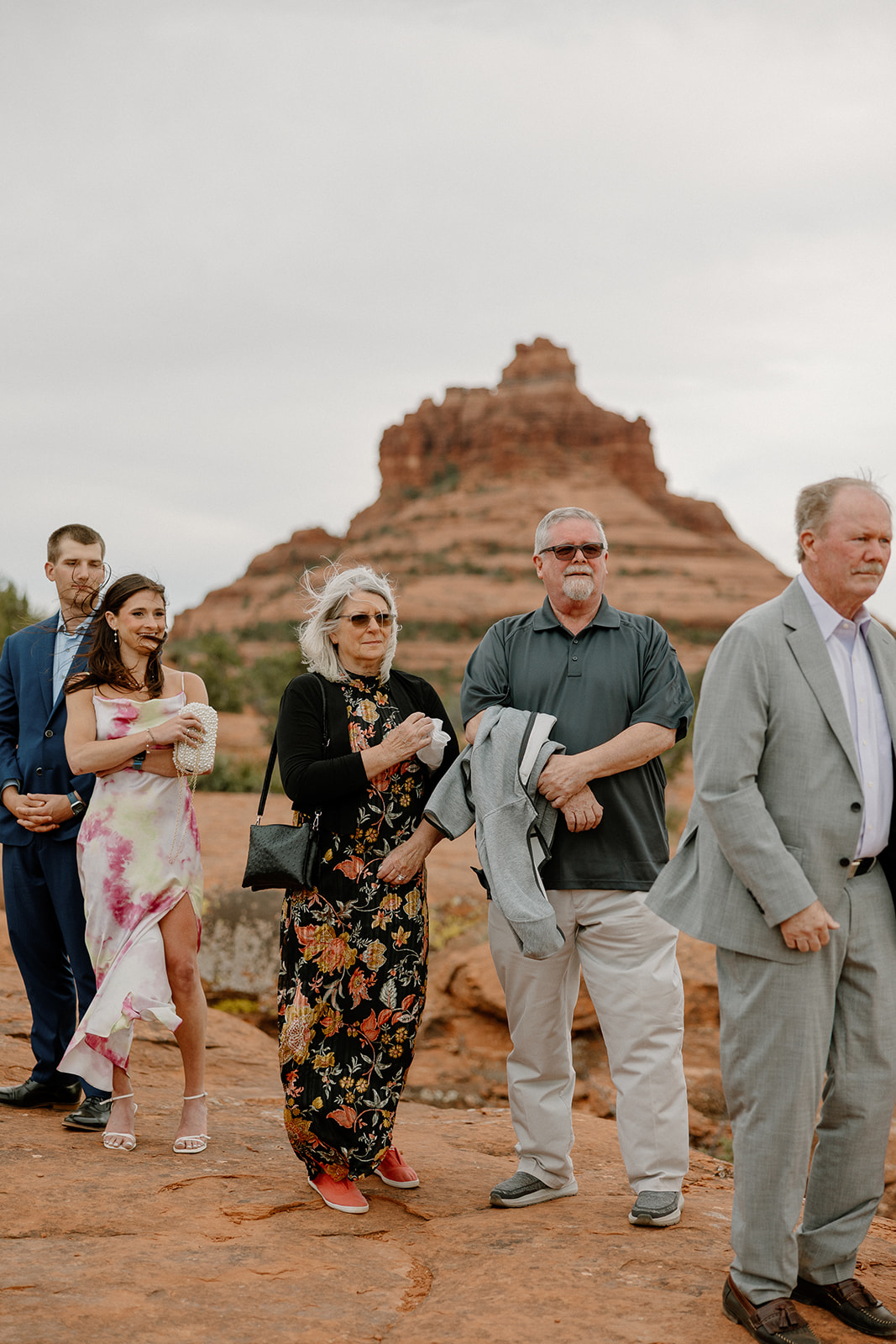 Guests gather on the red rocks for the ceremony, their expressions full of emotion as they look on in front of rust-colored cliffs.