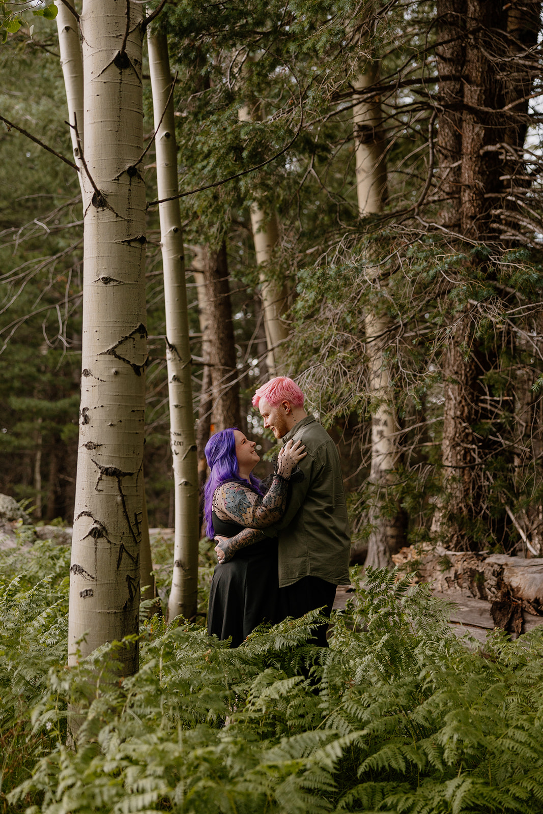 Candid moment of connection as the couple sits nestled in dense greenery, sharing an affectionate embrace—an example of forest-themed engagement photo ideas with texture and mood.