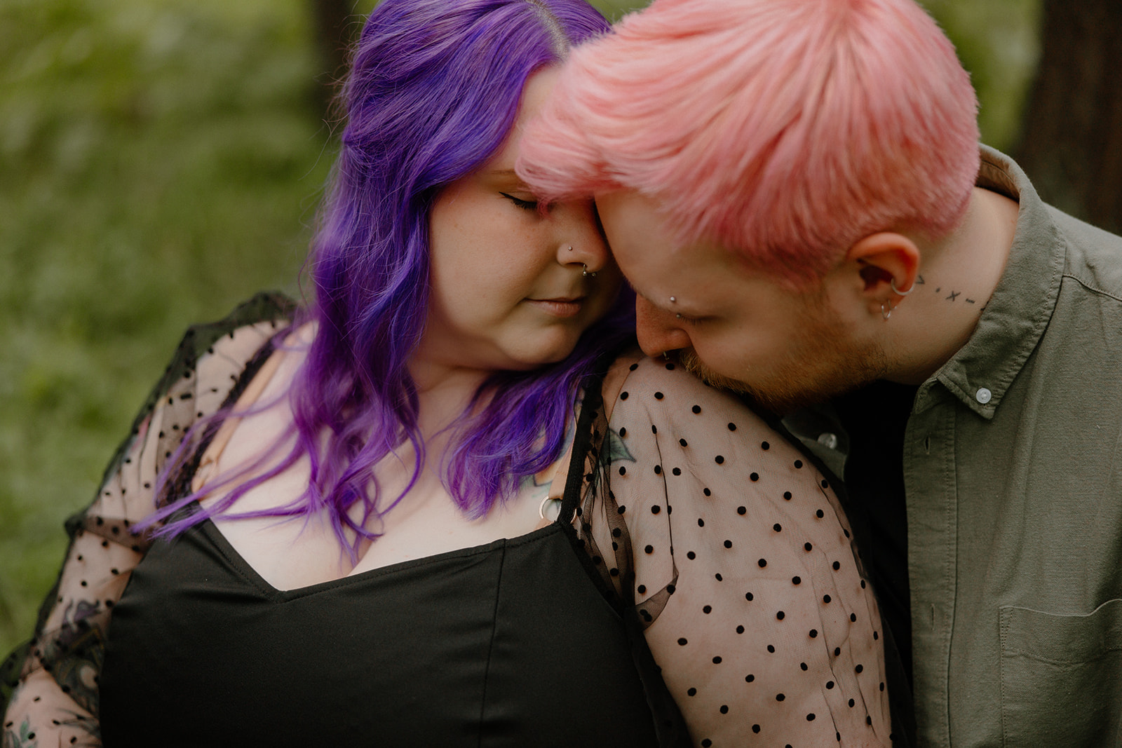 Close-up of a tender moment as the man kisses his partner’s shoulder, their colorful hair contrasting with the soft green backdrop—an intimate example of creative engagement photo ideas.