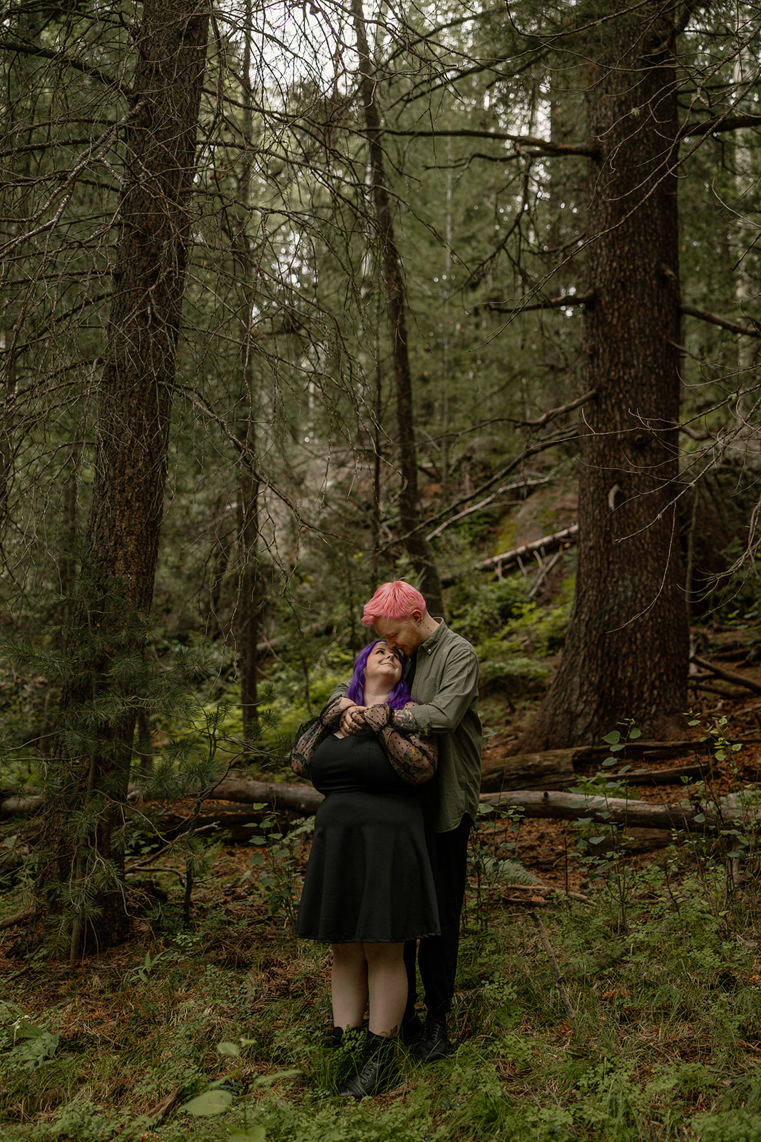 Wrapped in each other's arms, the couple stands quietly in a moody forest moment—perfect inspiration for emotional engagement photo ideas.