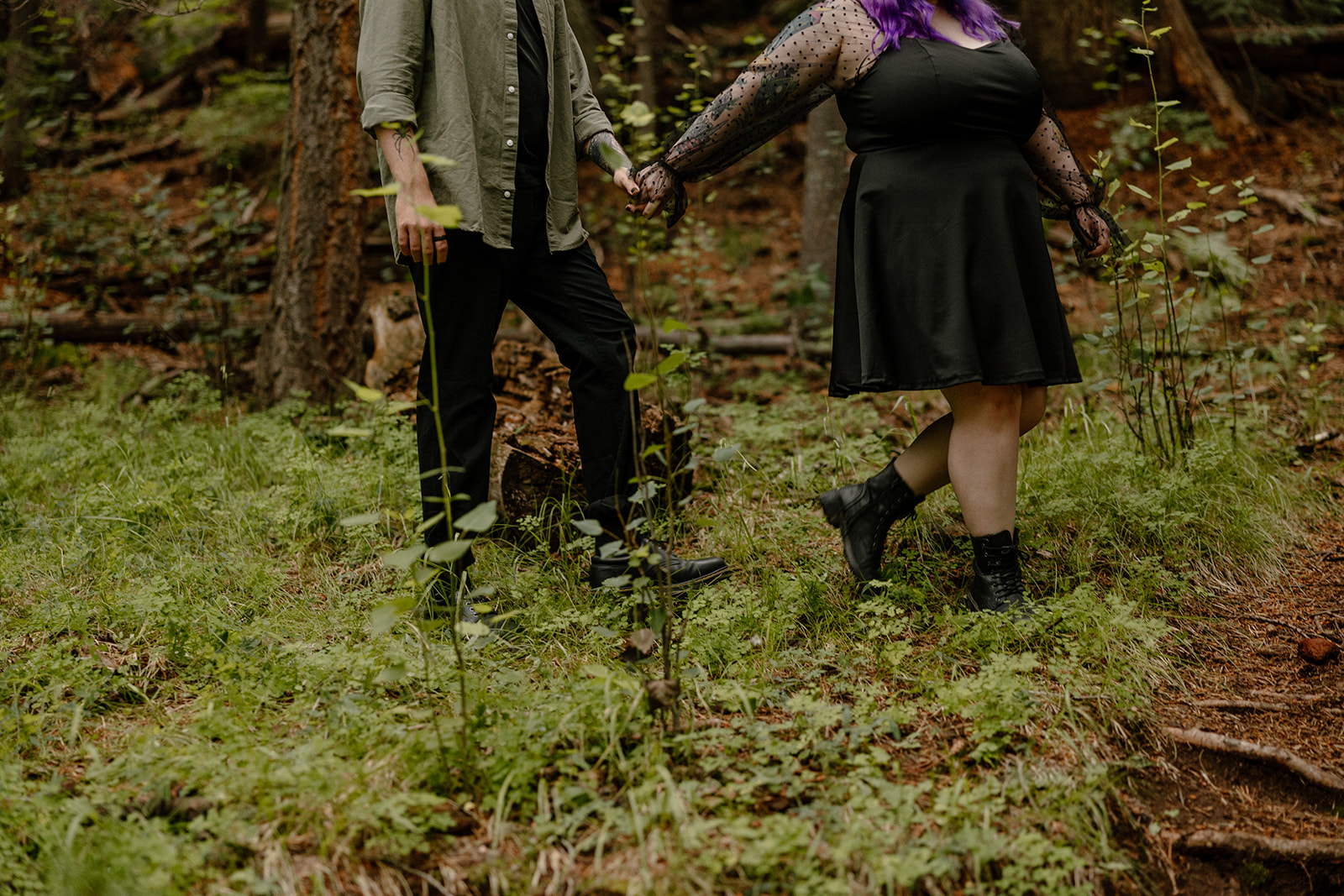 Close-up of intertwined hands and mid-step movement as the couple walks through forest undergrowth.