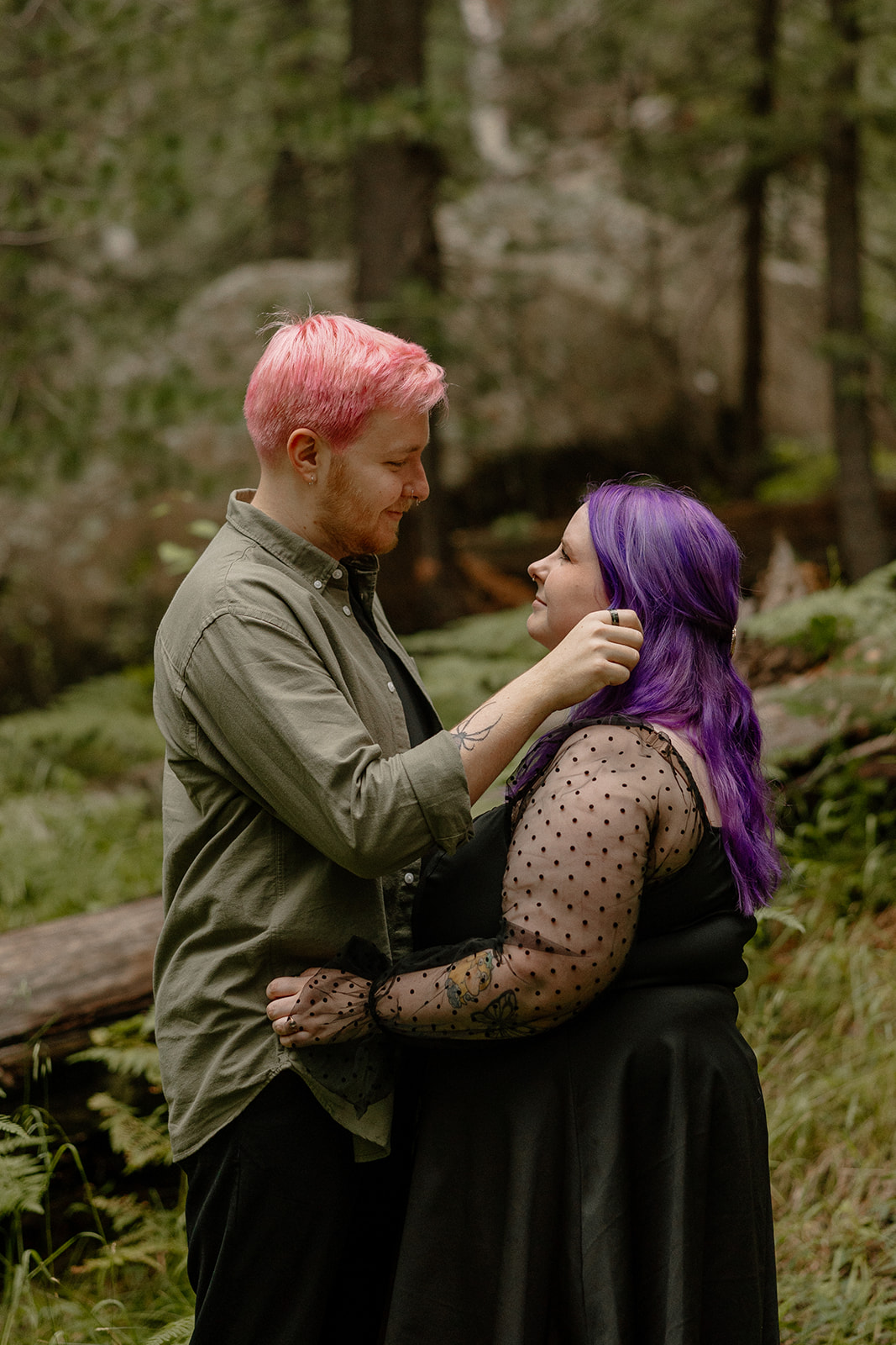 Close moment as a man gently brushes his partner’s hair back, with soft expressions and forest textures behind them—ideal for intimate engagement photo ideas.