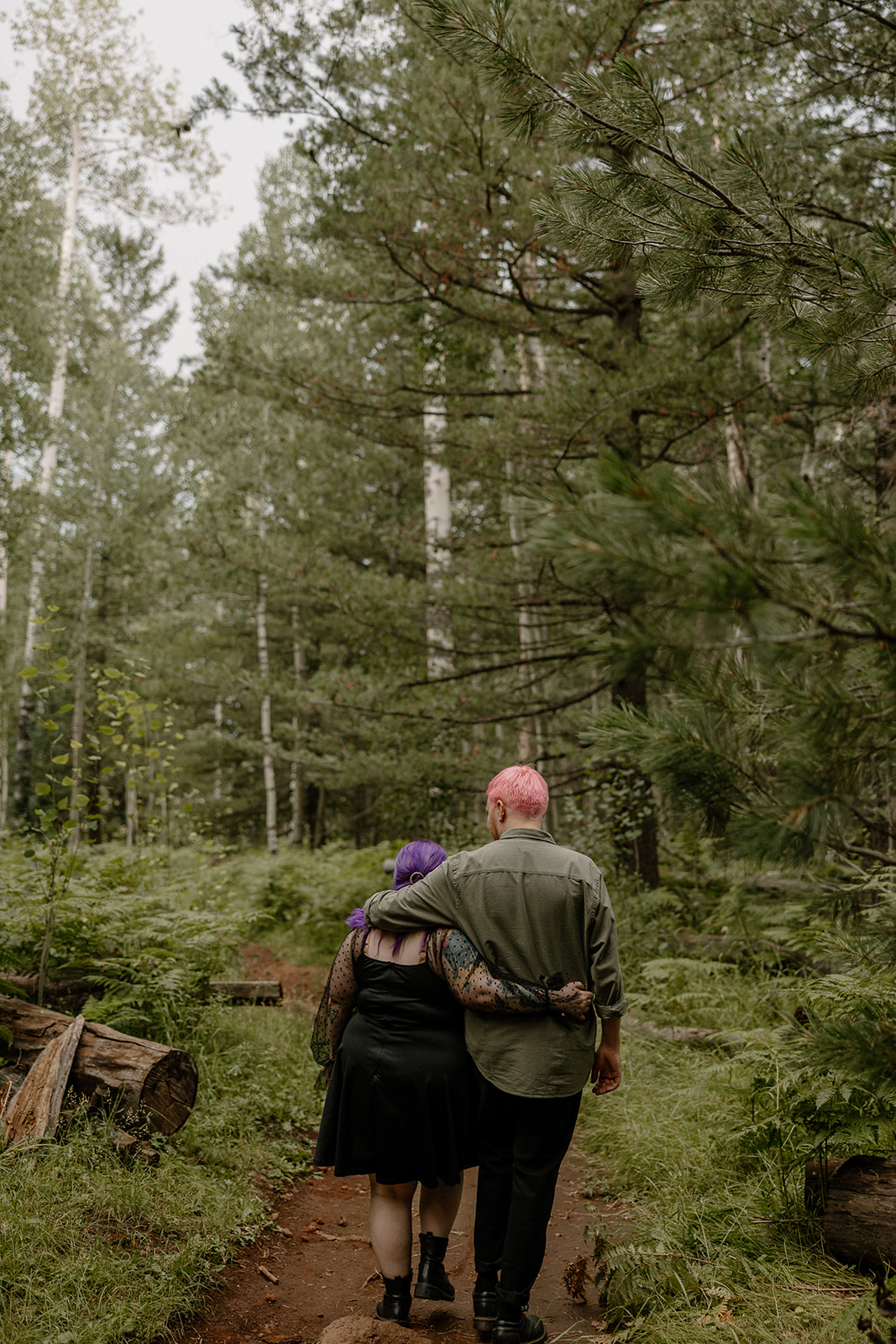 Arms wrapped around each other from behind, the couple walks down a forest path with a soft, romantic vibe.
