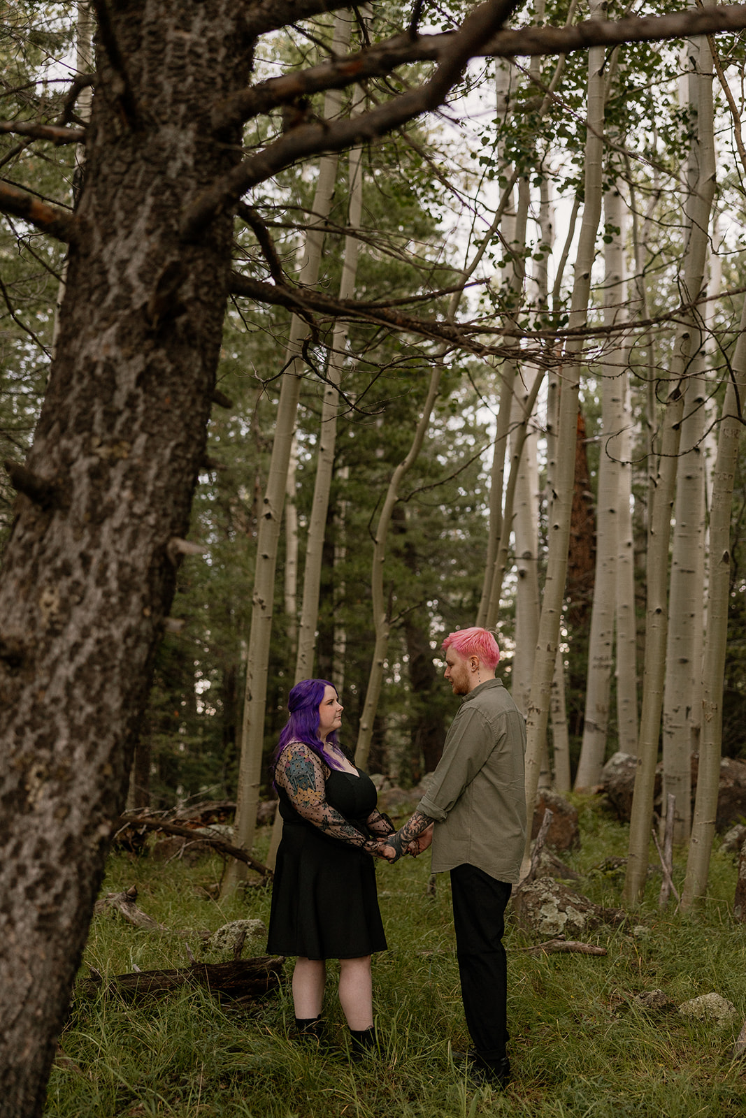 Two people face each other in a quiet forest clearing, holding hands among towering trees—beautifully simple engagement photo ideas in nature.