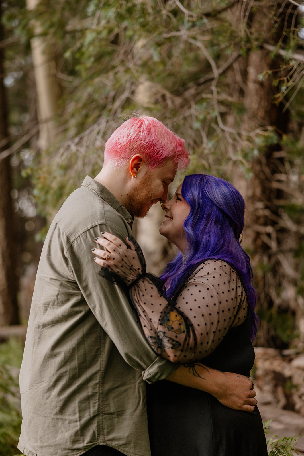 A close embrace in the woods, noses touching and eyes closed, with sunlight peeking through the trees.