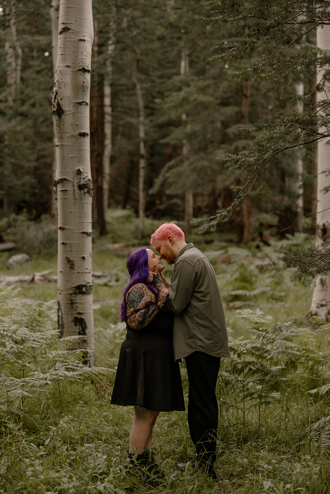 Intimate shot of a couple standing close, forehead to forehead, surrounded by towering trees—an ideal scene for unique engagement photo ideas.