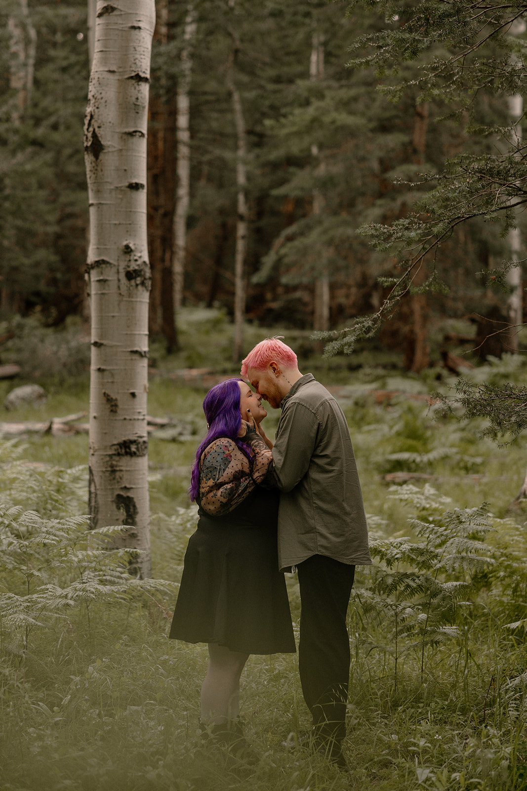 The couple stands forehead-to-forehead in a moment of stillness, surrounded by soft ferns and tall trunks—one of those emotional engagement photo ideas that hits just right.