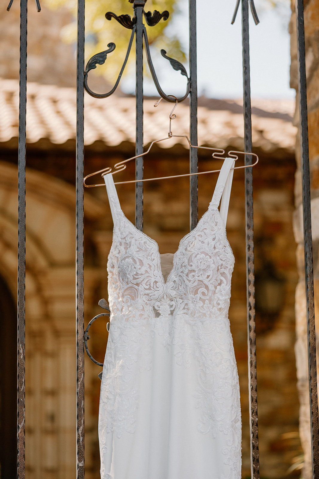 Lace wedding dress hanging from wrought iron gate with stone arches in the background at a Gilbert wedding venue.