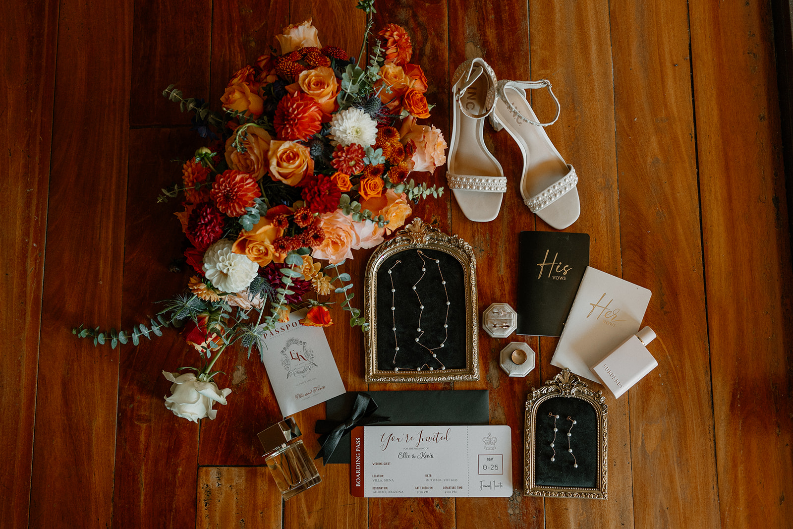 Flat lay of wedding details—bouquet, vow books, invitations, shoes, and constellation necklaces—styled on wood flooring.