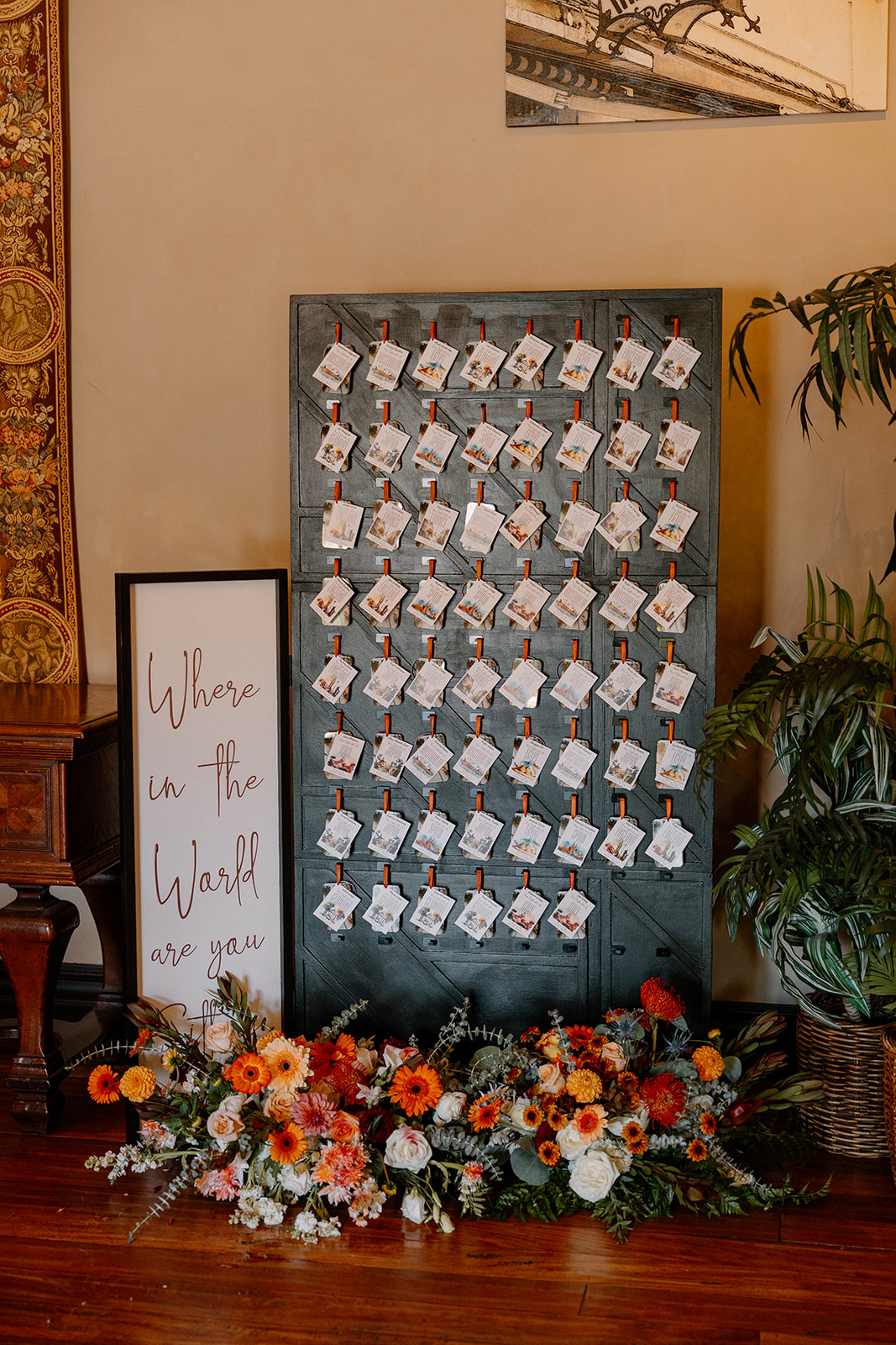 Where in the World Are You Sitting?” display with guest name cards, surrounded by lush floral arrangements in an indoor wedding space.