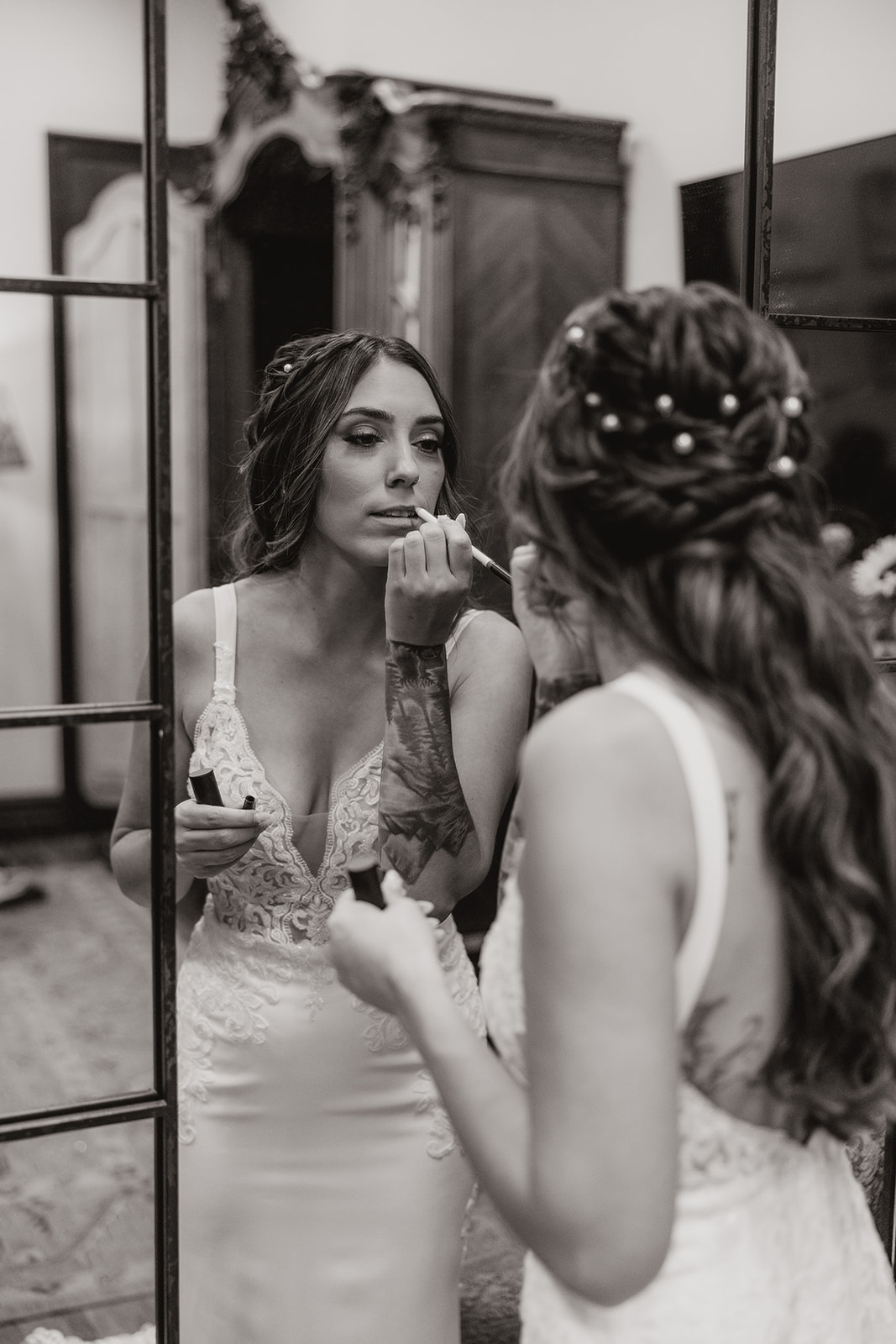 Black and white image of bride applying lipstick in front of a tall mirror before the ceremony.