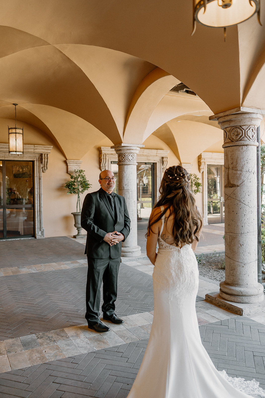 Father seeing his daughter in her wedding dress for the first time beneath stone archways with warm natural light.