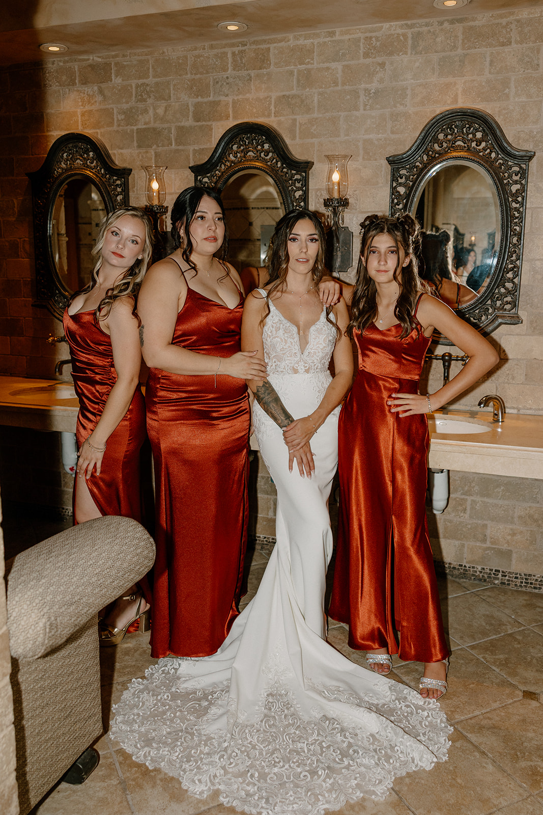 The bride poses with her bridesmaids in a luxe, tile-accented dressing room with antique mirrors and dramatic lighting.