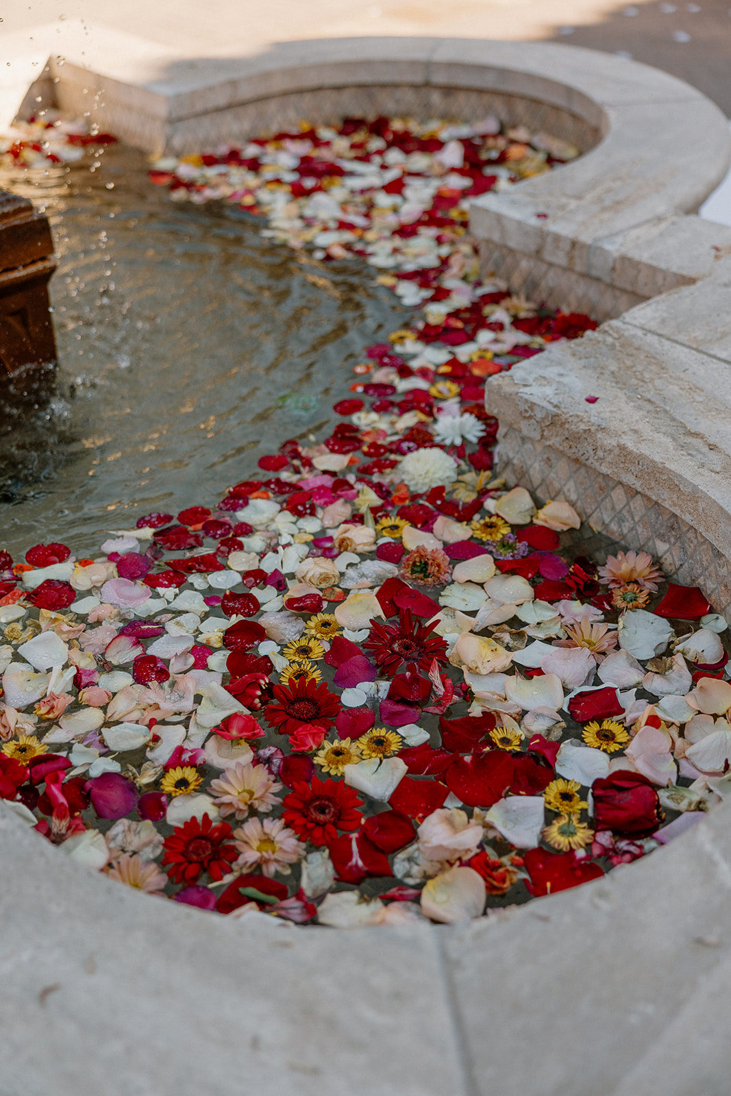 A curved stone fountain filled with floating rose petals and wildflowers, adding a soft, whimsical detail to the venue décor.