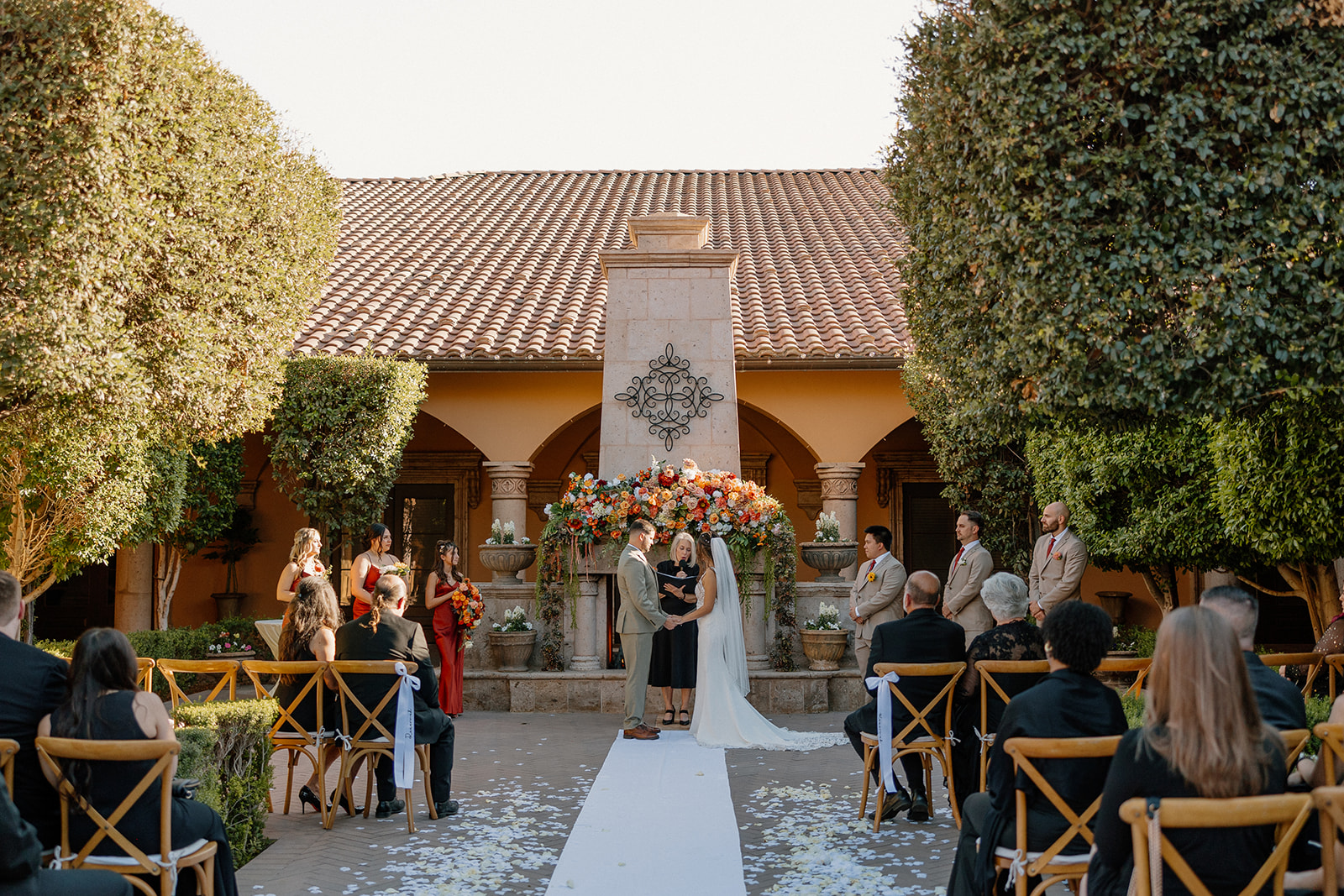 Courtyard wedding ceremony at a Gilbert wedding venue with floral altar, terracotta walls, and late afternoon light.