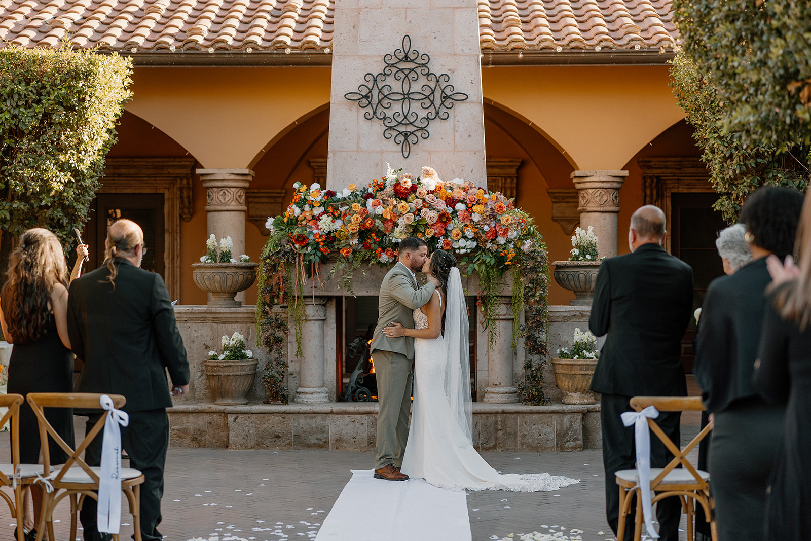 Bride and groom share their first kiss under a stunning floral arch built onto a stone fireplace at a romantic Gilbert wedding venue.