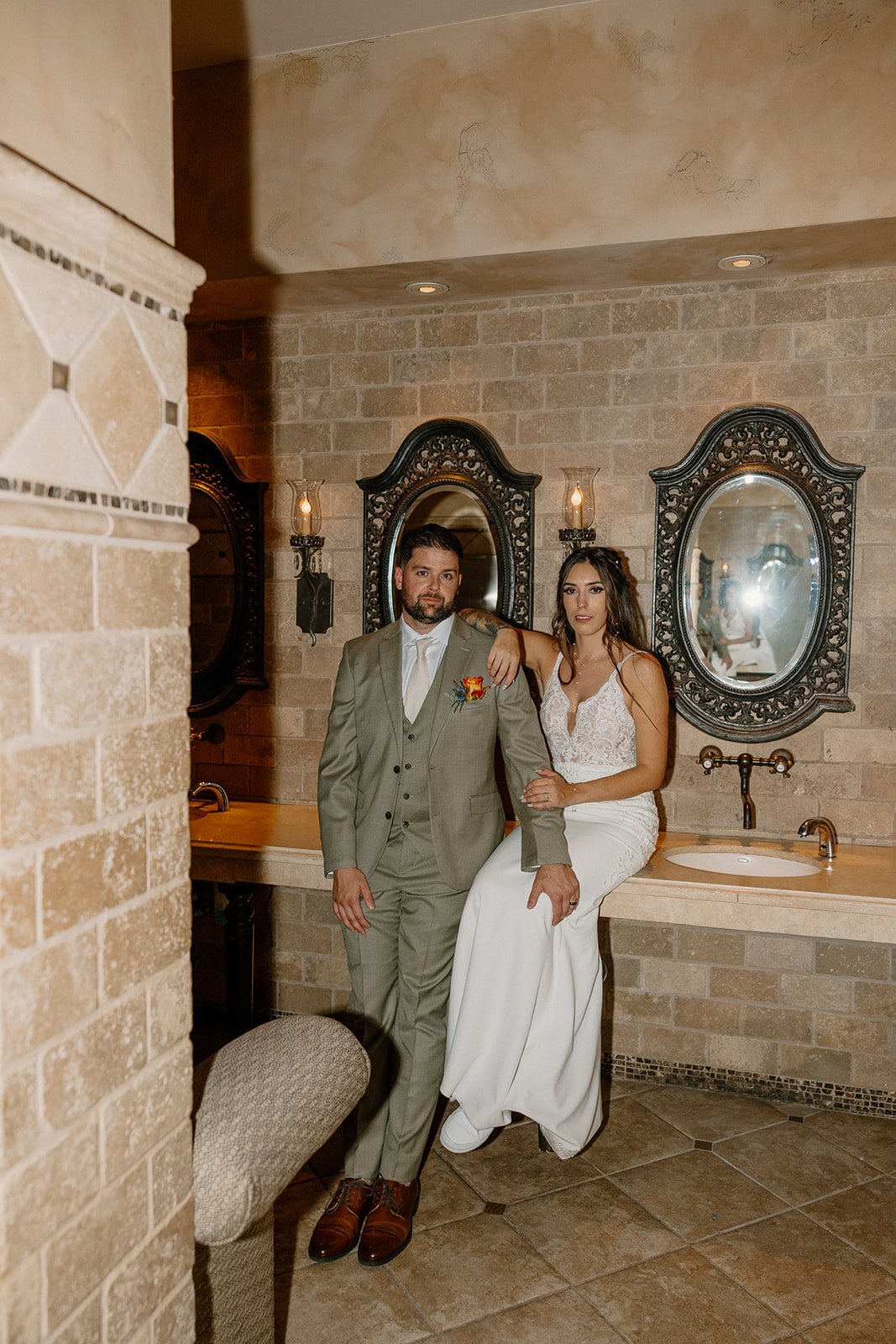 The bride and groom pose in a tiled room with ornate mirrors and stone walls, a unique moment captured in an unexpected space.