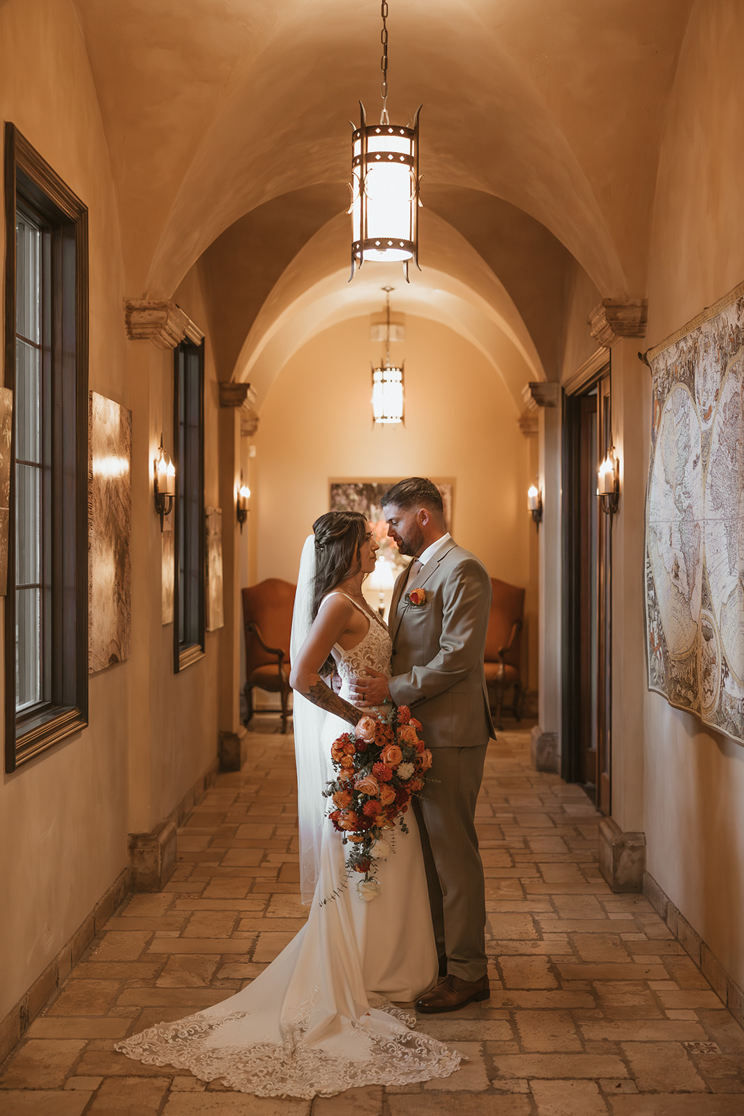 Bride and groom share a quiet moment inside a softly lit hallway with arched ceilings and warm-toned walls.