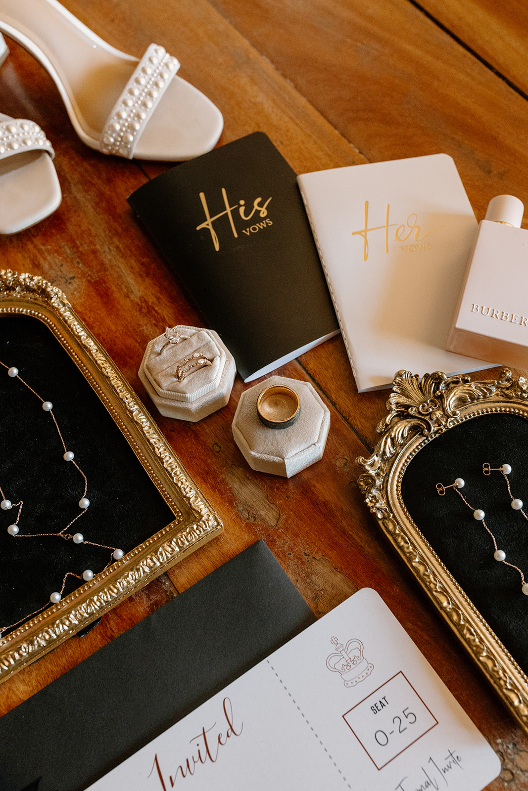 Close-up of wedding day flat lay details including vow books, rings, and constellation jewelry on a wood surface.