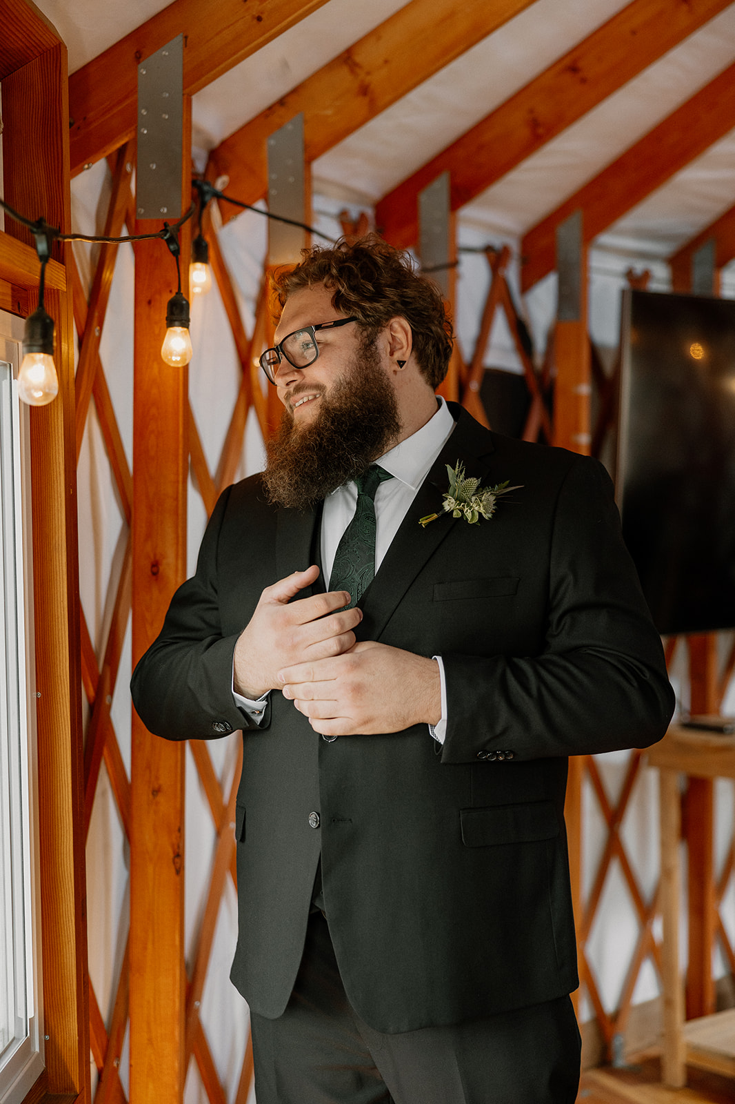 Groom buttoning up his suit jacket beside a wood-burning stove inside a yurt at Nordic Village AZ.