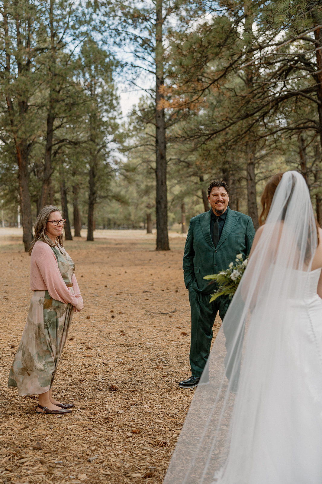 Bride standing in the forest with her parents, sharing a quiet moment before the ceremony.