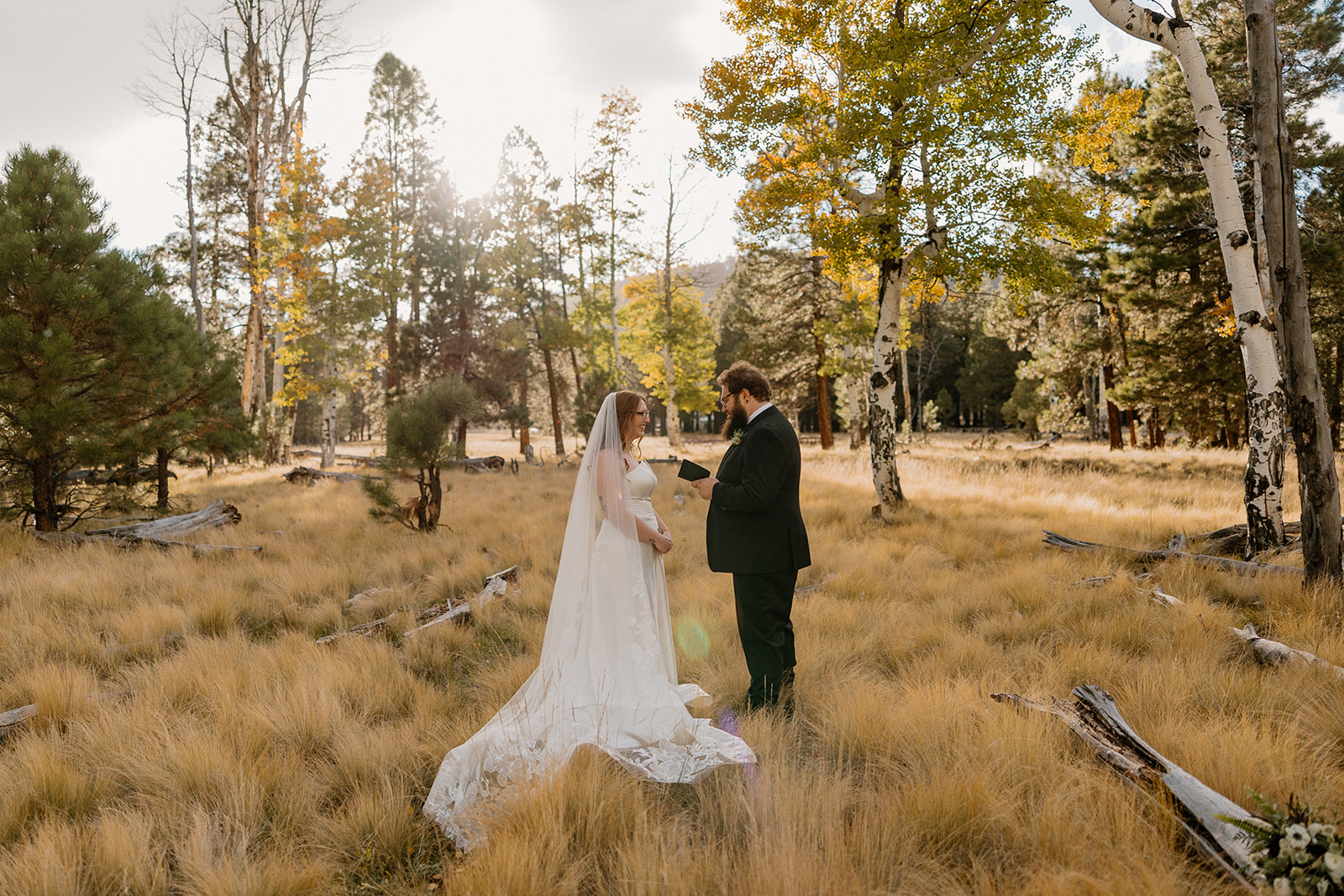 Intimate moment as the bride adjusts her groom’s boutonniere in a golden grass meadow.