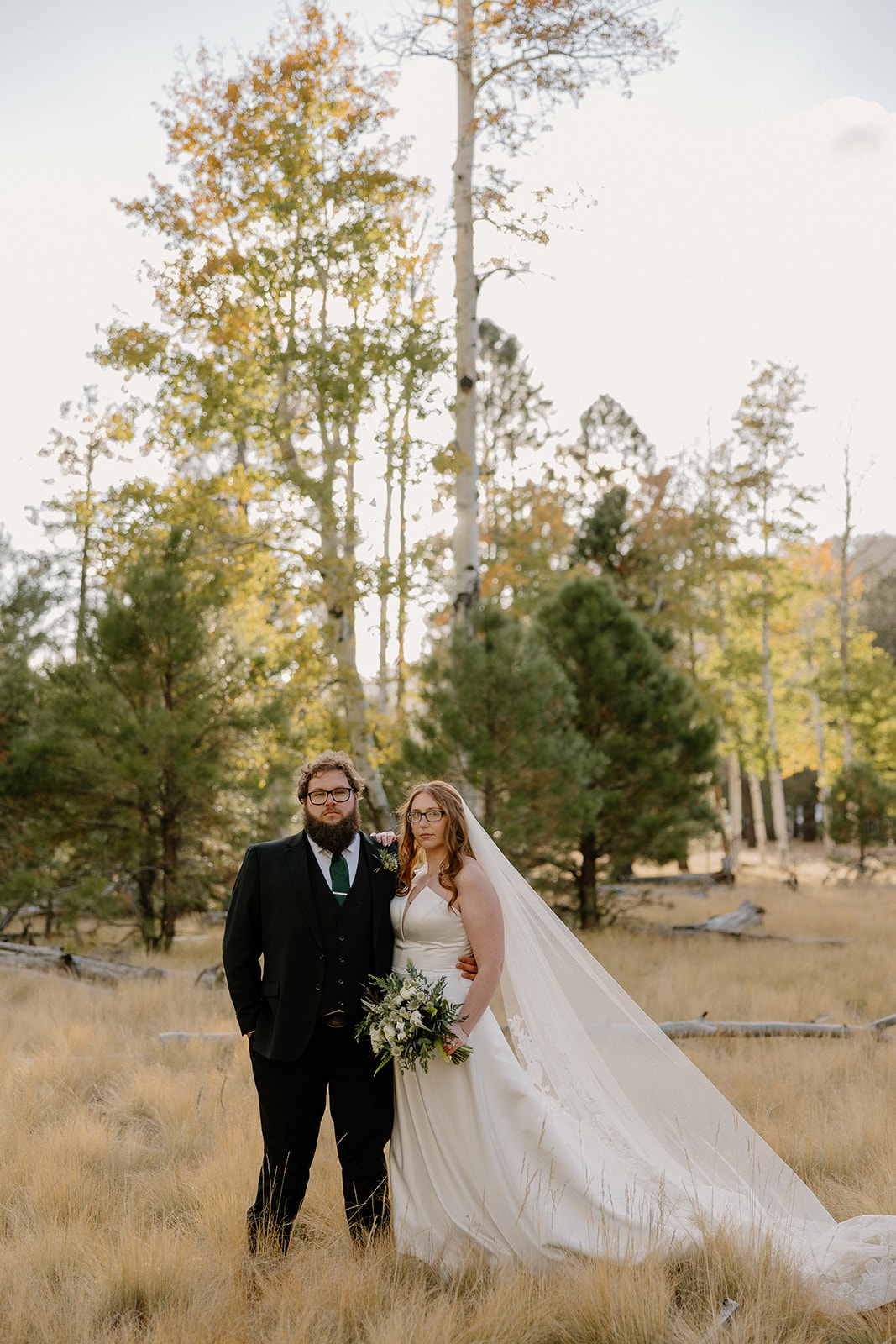Bride raises her bouquet in celebration as she and her groom walk hand-in-hand down a wooded path post-ceremony.
