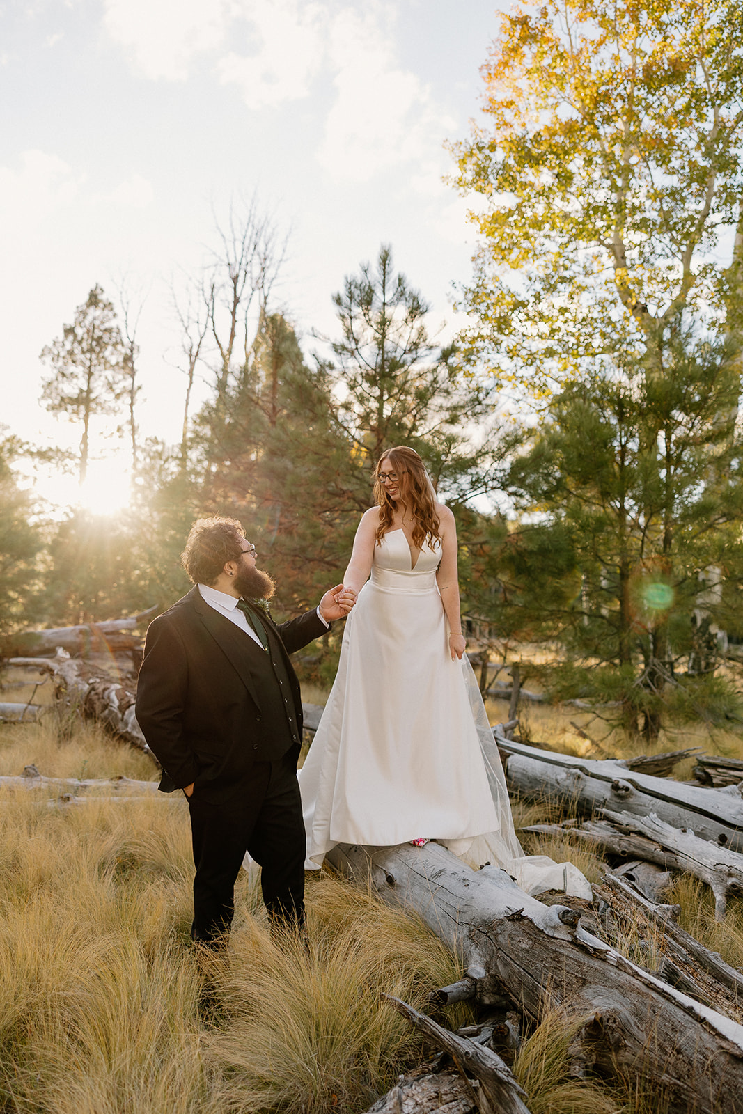Groom lifts the bride in a joyful embrace among golden grasses and pine trees during their forest wedding celebration.