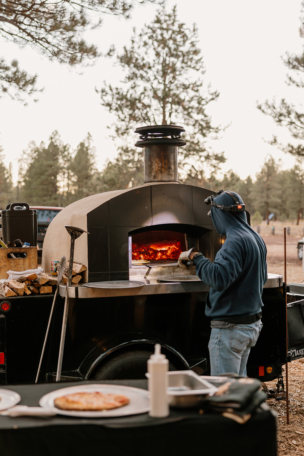 Outdoor wood-fired pizza oven blazing while a chef tends to the flames—casual, cozy catering at Nordic Village AZ.