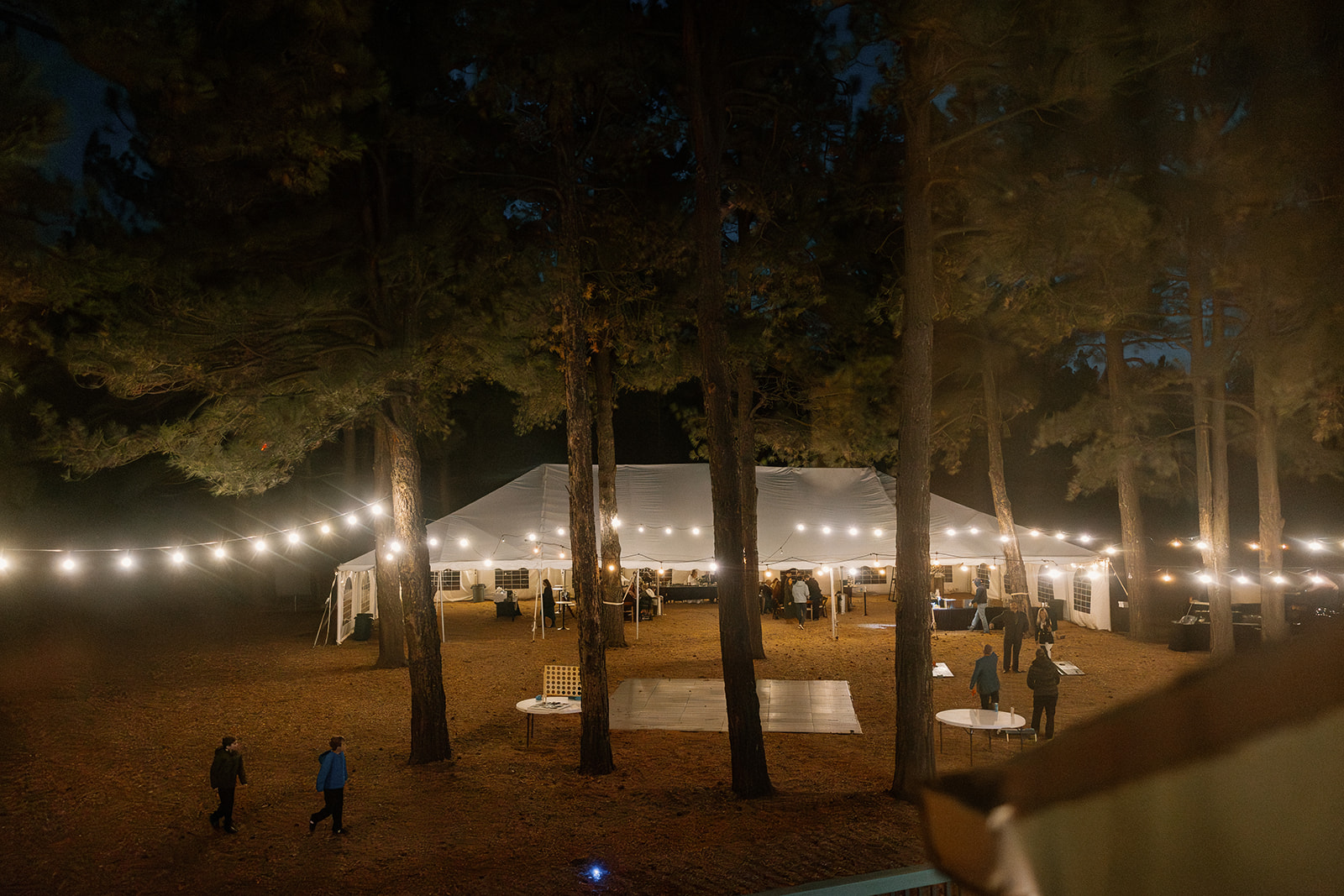 Twinkle lights stretch through tall pine trees around the glowing white reception tent at Nordic Village AZ during the evening celebration.
