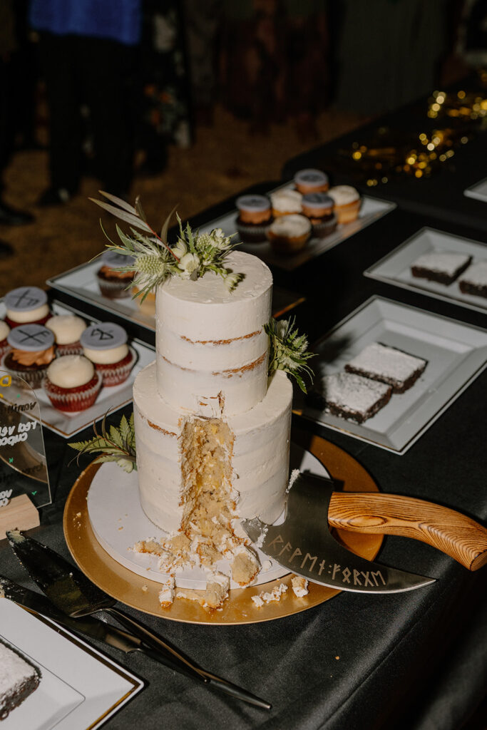 Sliced wedding cake with floral accents and Norse-inspired cake server, surrounded by cupcakes and dessert trays at Nordic Village AZ.