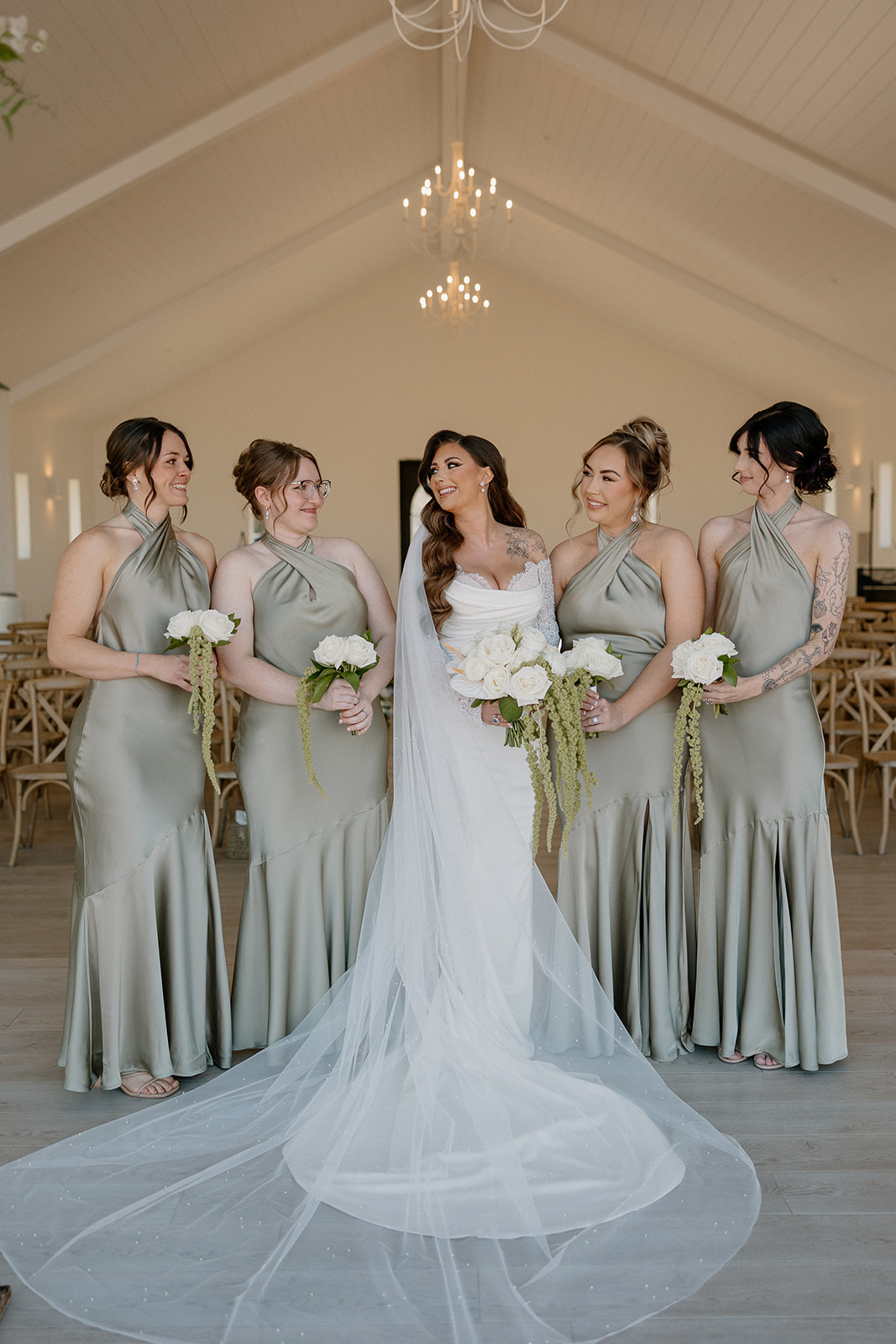 Classic wedding party portrait with the bride and bridesmaids in soft green satin dresses inside a modern venue.