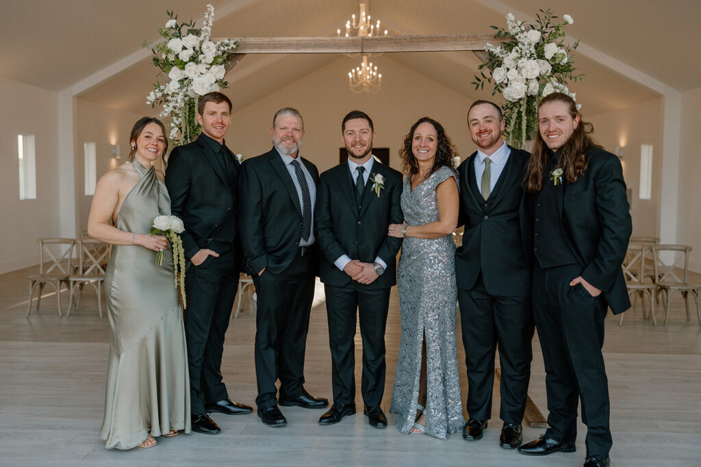 Group portrait of the groom with family and friends in a minimal indoor chapel space.