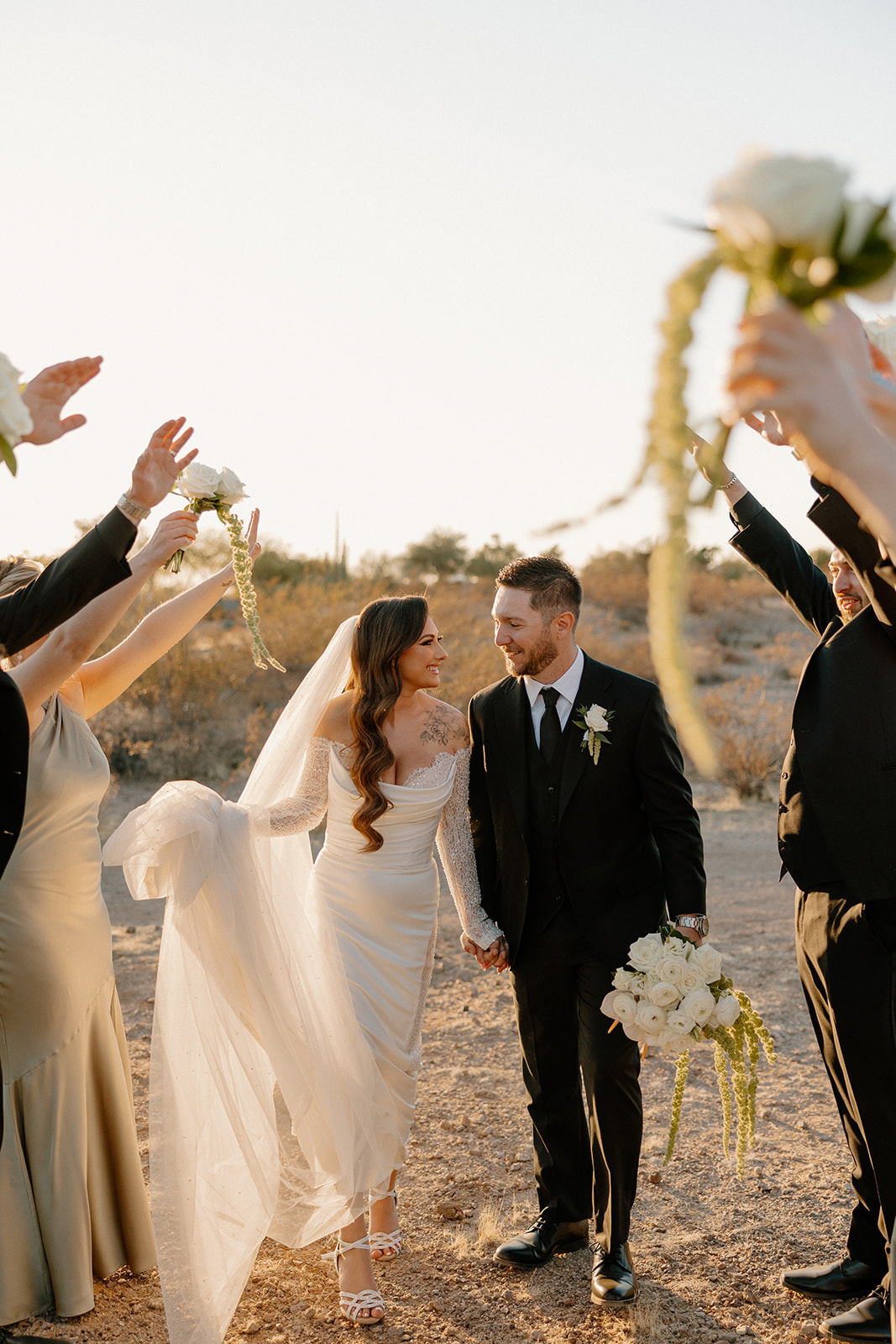 Playful walk through cheering bridal party as guests raise bouquets around the couple.