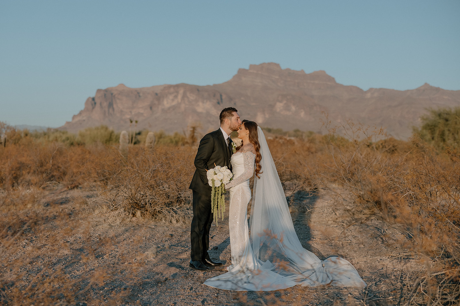 Desert wedding portrait with bride and groom kissing in front of Arizona red rock mountains — a perfect scene for any wedding planning guide.