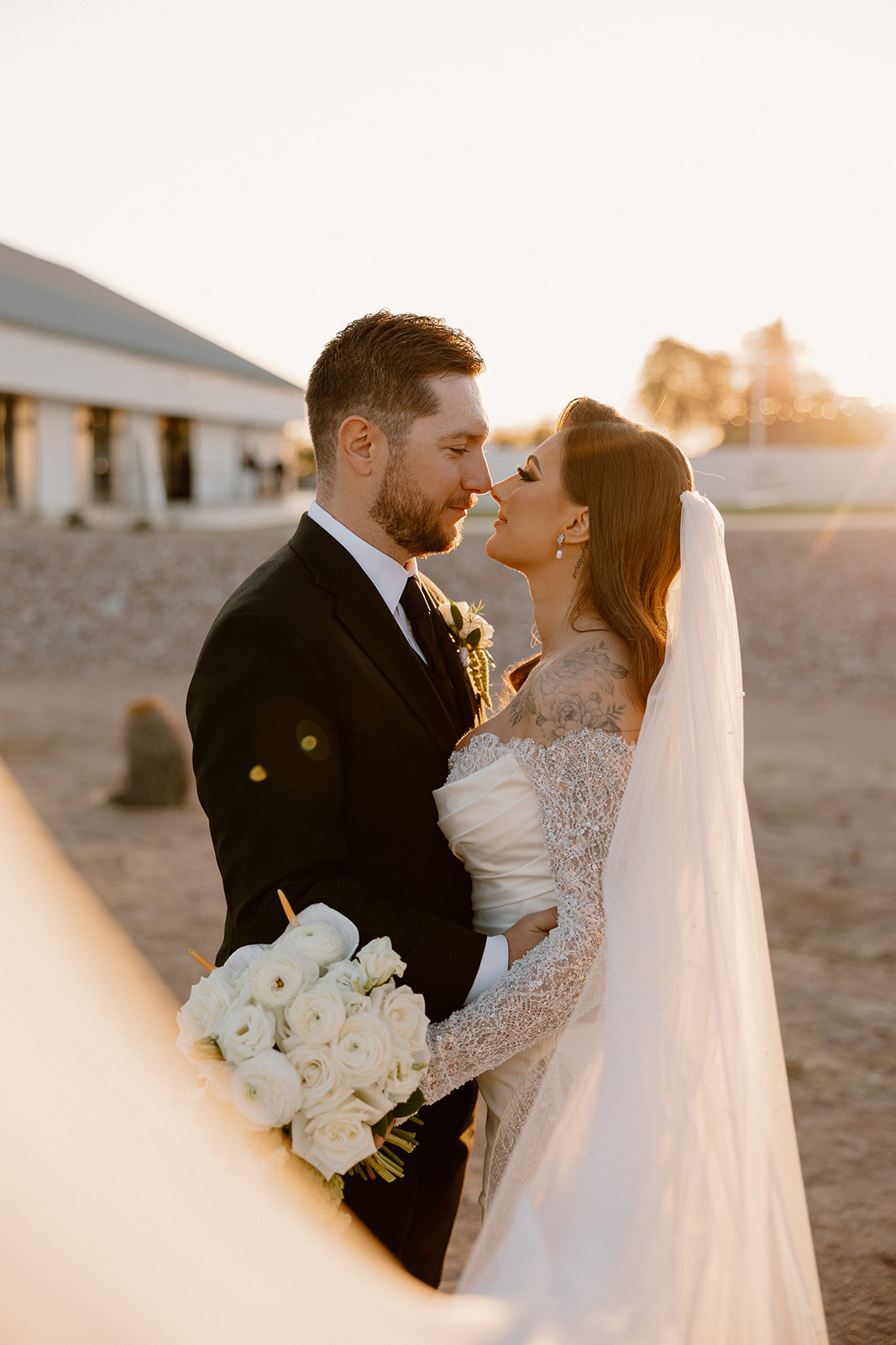 Bride and groom in a golden hour portrait with bouquet detail and soft flowing veil.