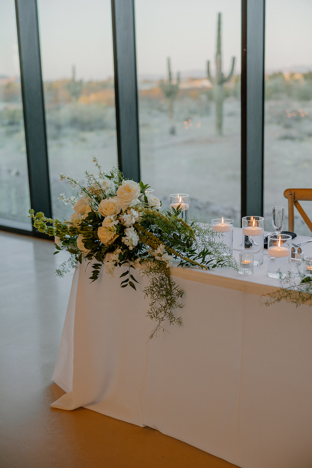 Minimal modern sweetheart table with romantic candle glow, greenery, and soft florals in front of a desert view.