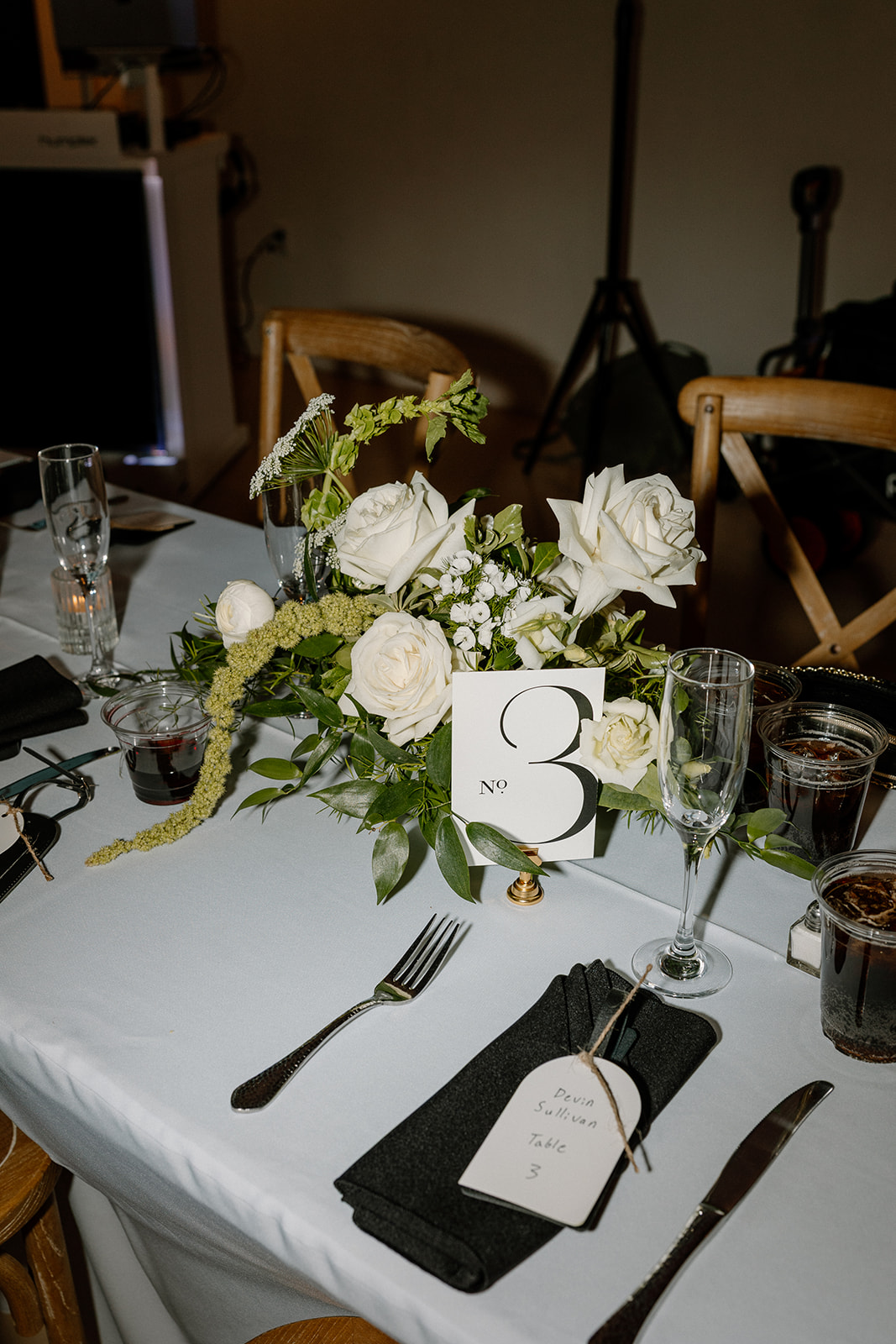 Elegant white rose centerpiece with table number and name card on a black-and-white reception table — a classic detail for your wedding planning guide.