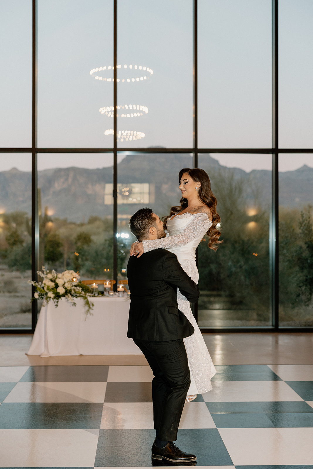 Romantic lift during first dance in a modern desert venue, surrounded by soft light and mountain silhouettes.