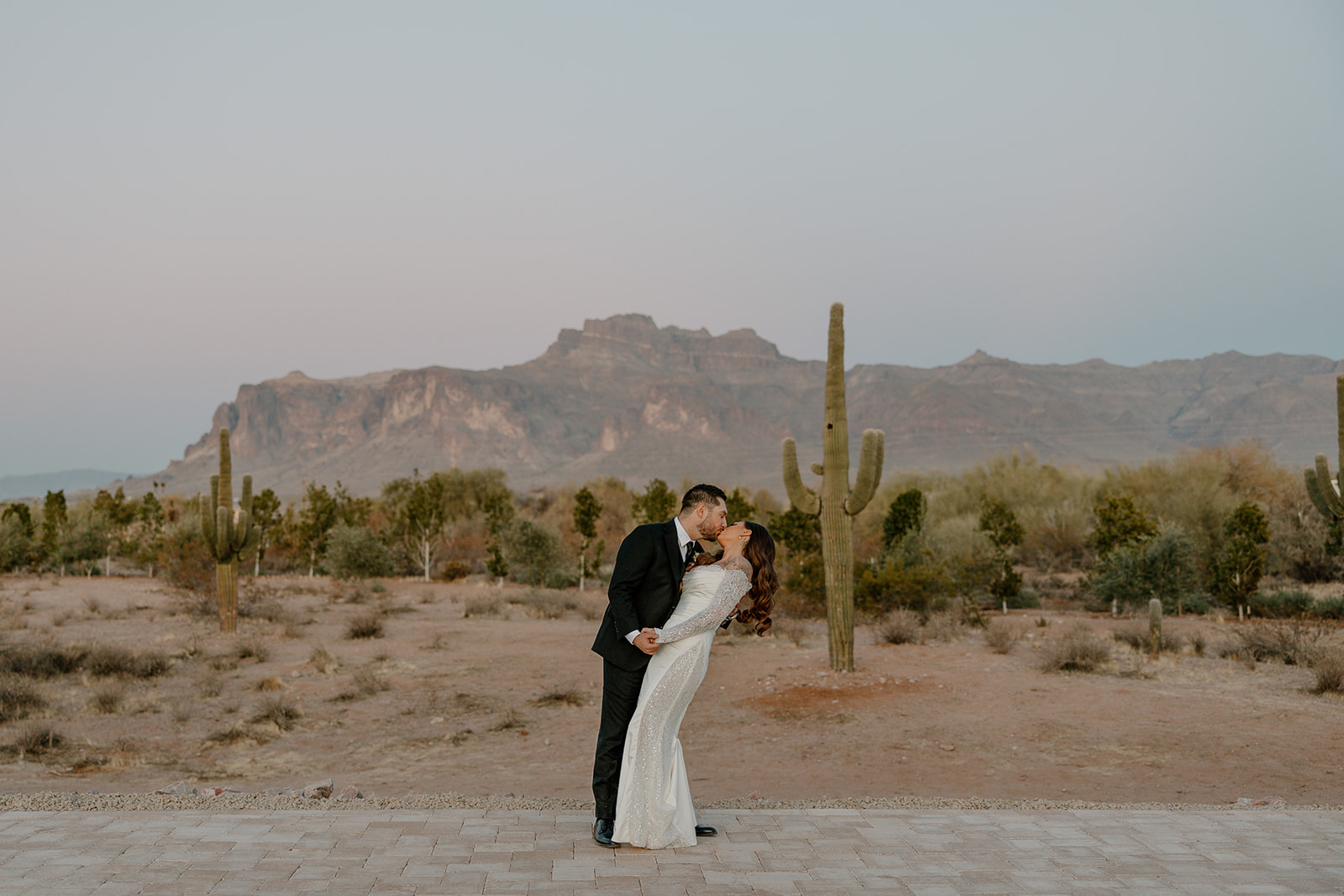 Groom dips the bride for a kiss as the desert stretches behind them, Superstition Mountains glowing in the soft evening light at a desert view wedding venue.