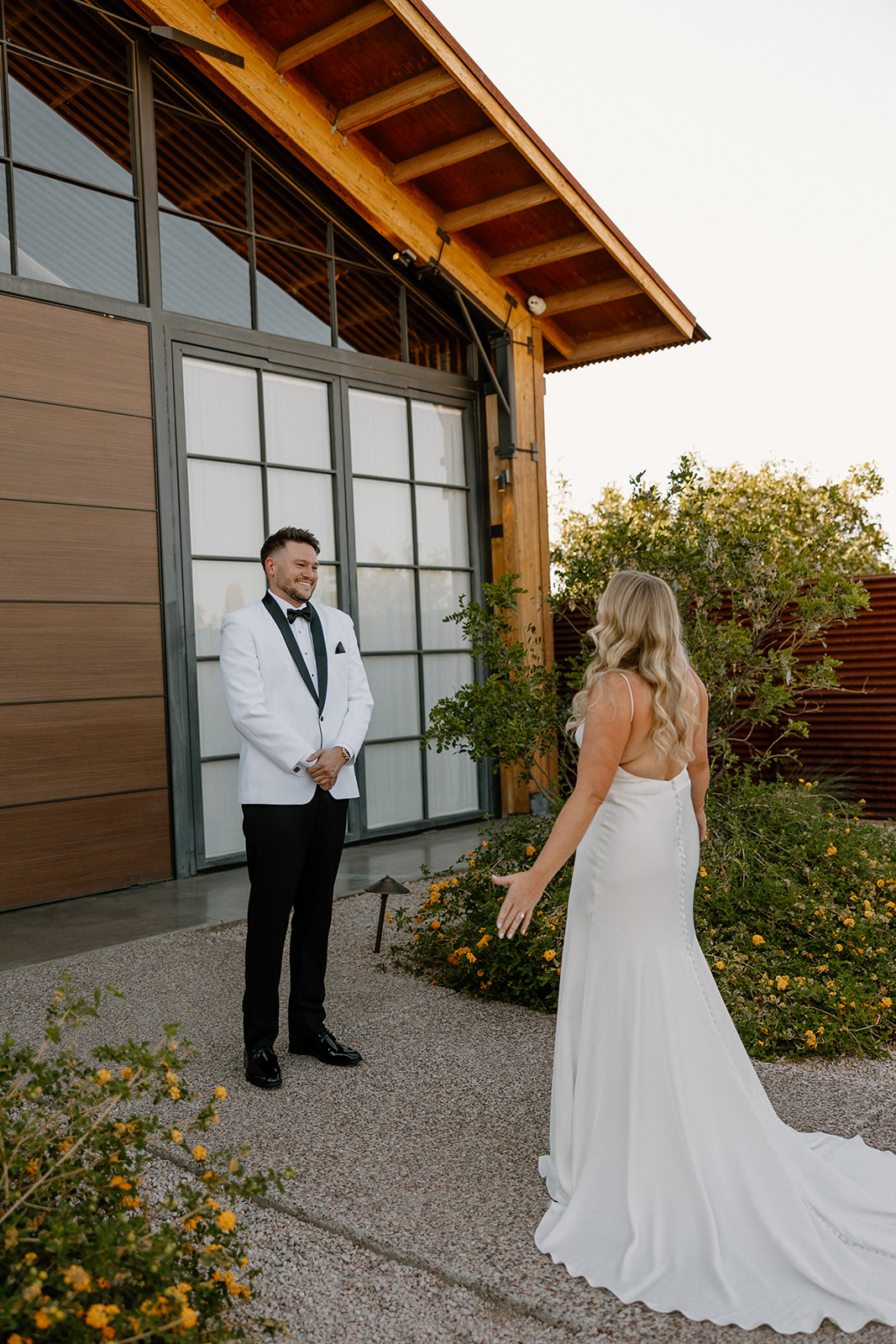 Groom’s emotional first look as the bride approaches in her wedding gown outside a modern desert venue.