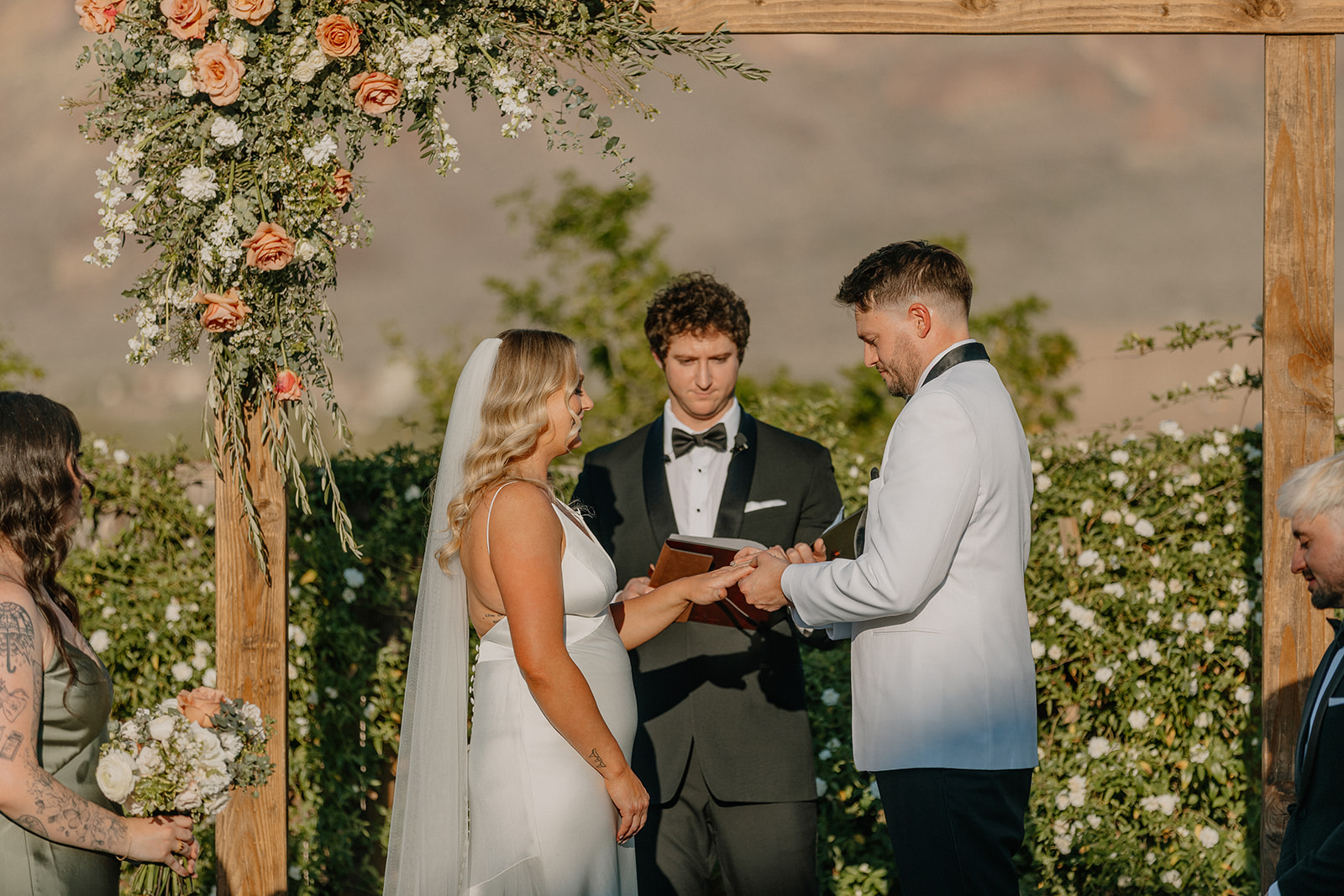 Bride and groom exchanging rings under a floral arch during their outdoor ceremony at one of the most romantic wedding venues in Arizona.